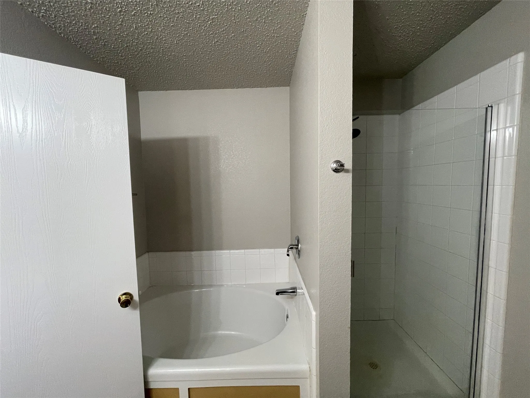 Built-in soaking tub with white tile surround, glass-enclosed shower, and chrome fixtures