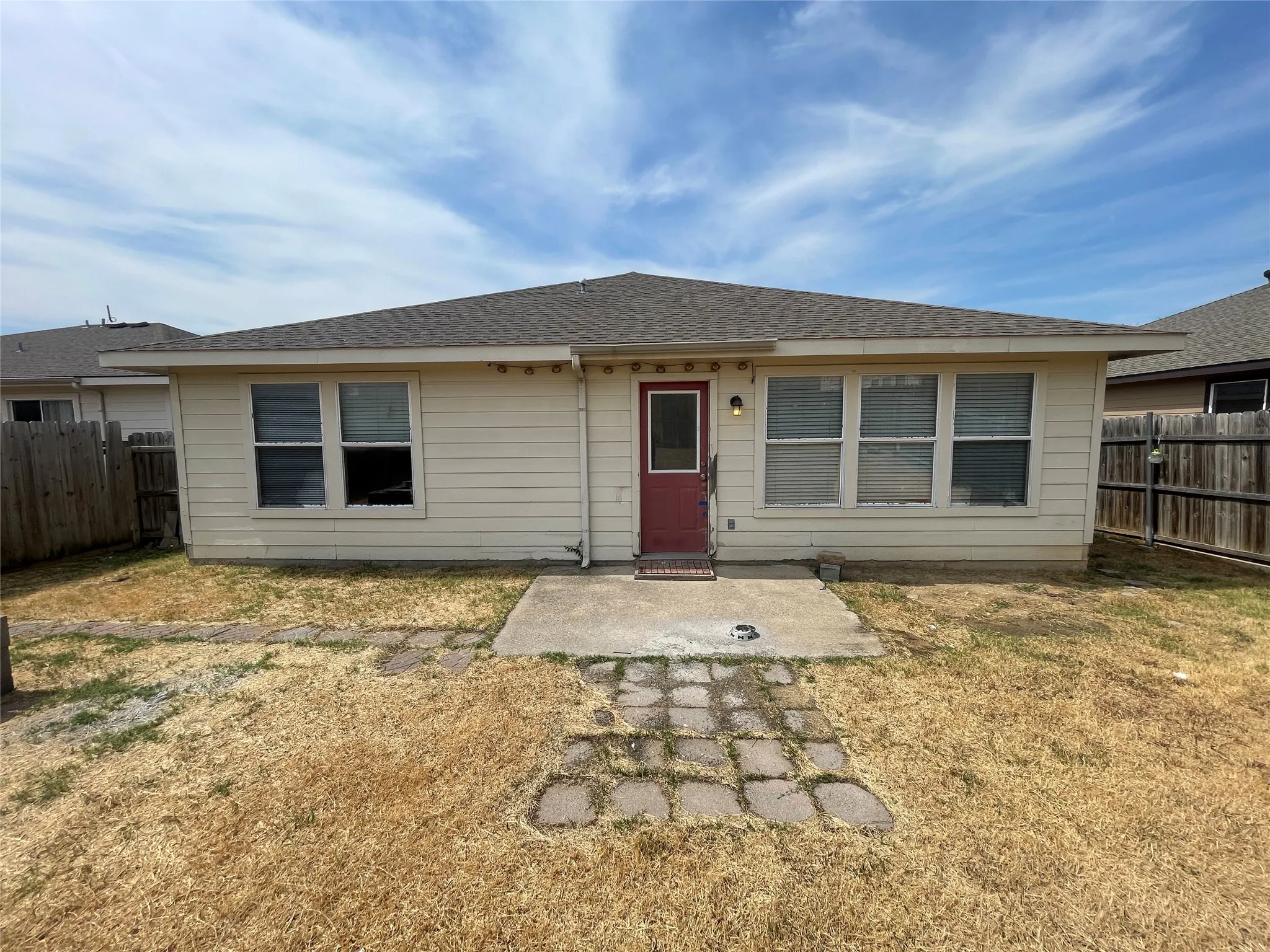 Rear exterior featuring a red entry door, multiple windows, a concrete patio, and a shingled roof