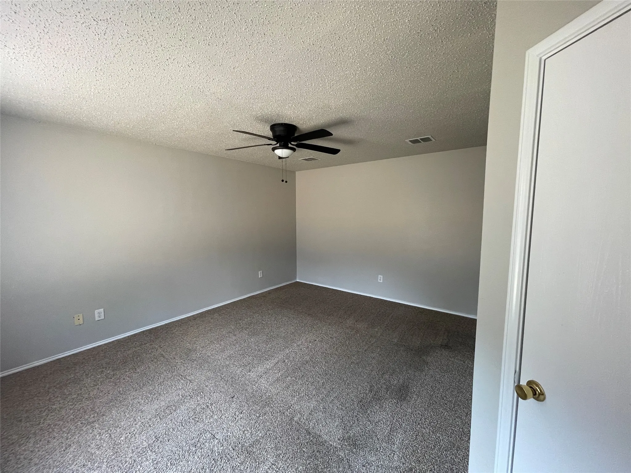 Neutral wall color, textured ceiling, carpeted flooring, and a ceiling fan with integrated lighting