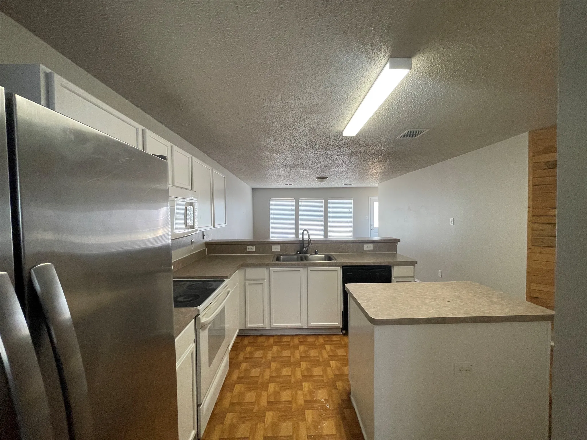 Kitchen featuring white cabinetry, light countertops, wood-finish flooring, and a stainless steel refrigerator