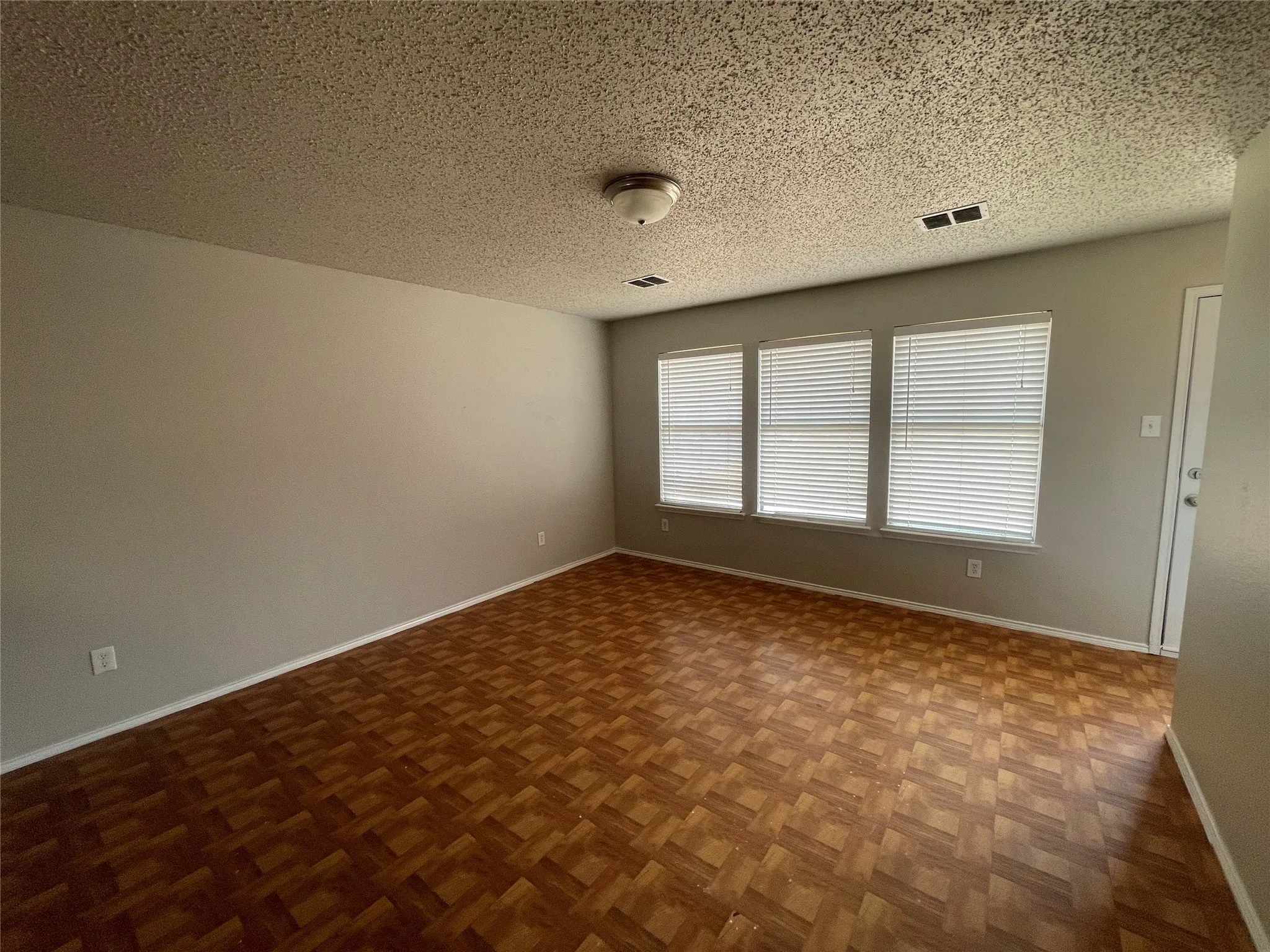 Wood-finish flooring, three windows with blinds, and light neutral wall paint