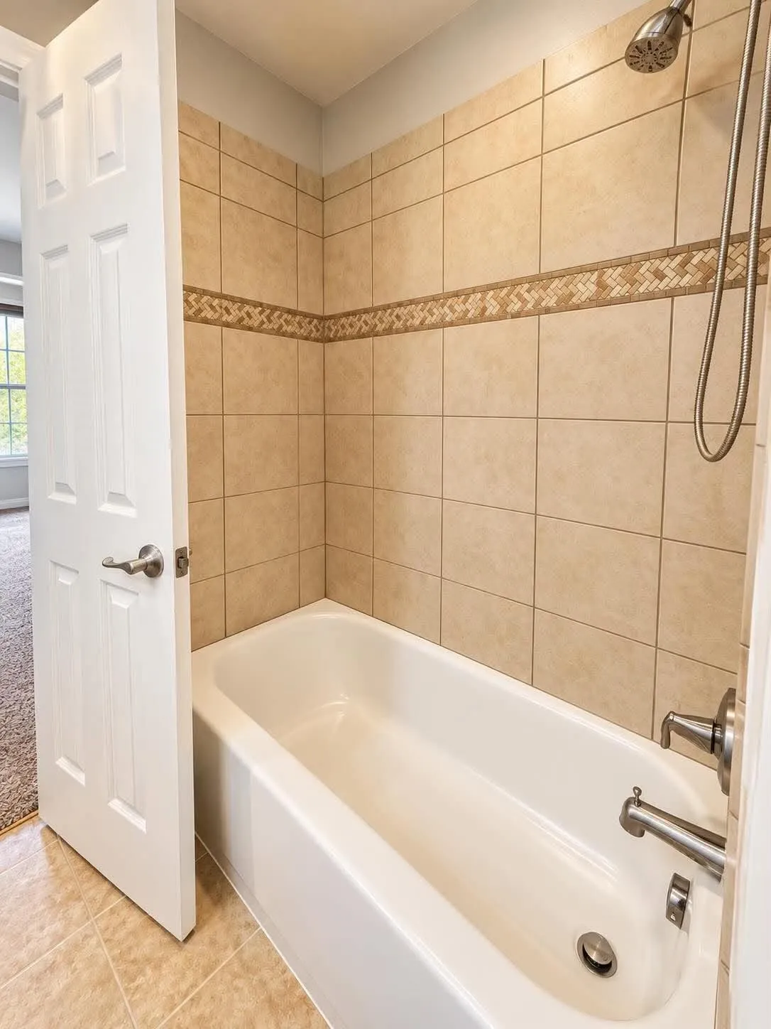 Bathtub with tiled surround, decorative accent tile band, and a brushed nickel shower head
