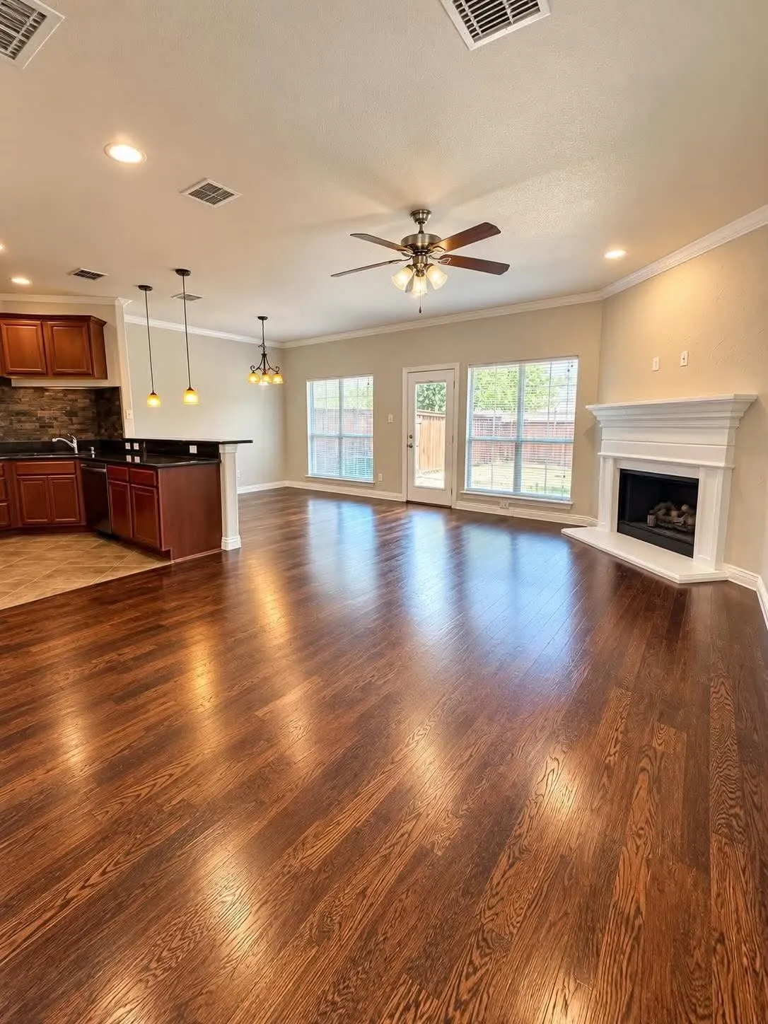 Expansive wood-finish flooring, white crown molding, and a fireplace with a mantel