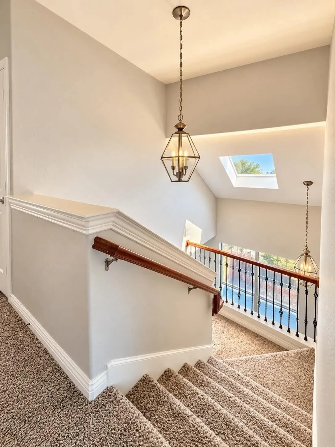 Carpeted staircase with a wood handrail, wrought iron balusters, and a skylight