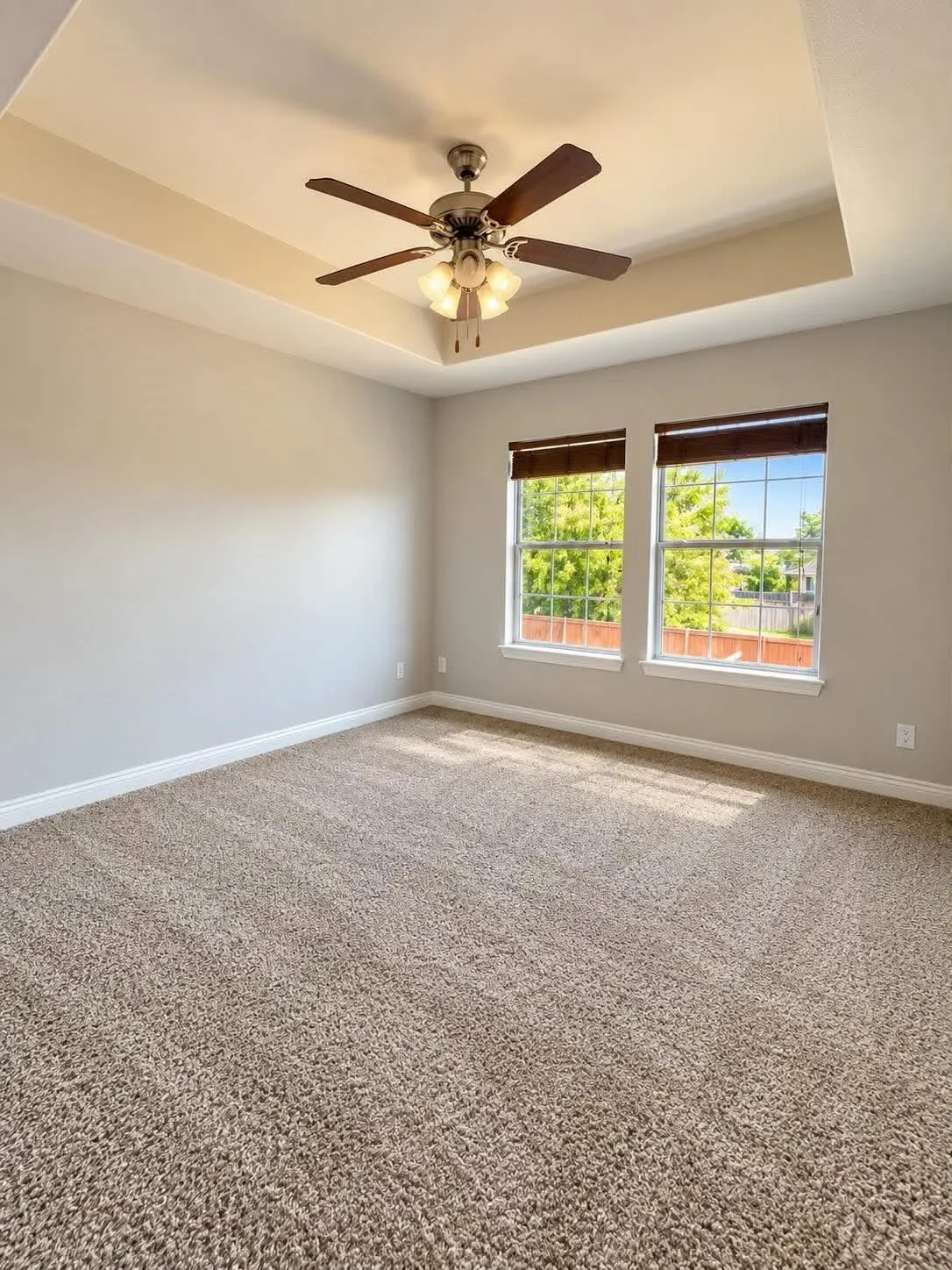 Tray ceiling with an attached ceiling fan and light fixture, two windows with blinds, and wall-to-wall carpeting