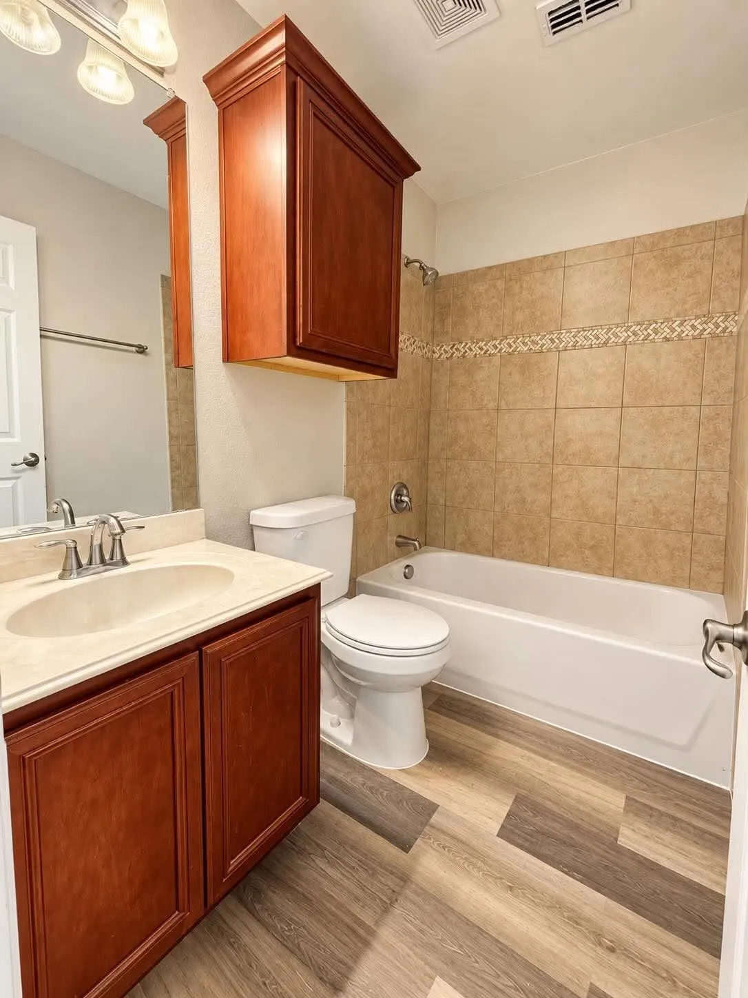 Wood-finish flooring, a vanity with a light-colored countertop and integrated sink, a built-in wood-toned storage cabinet, a bathtub with a tiled surround, and a toilet