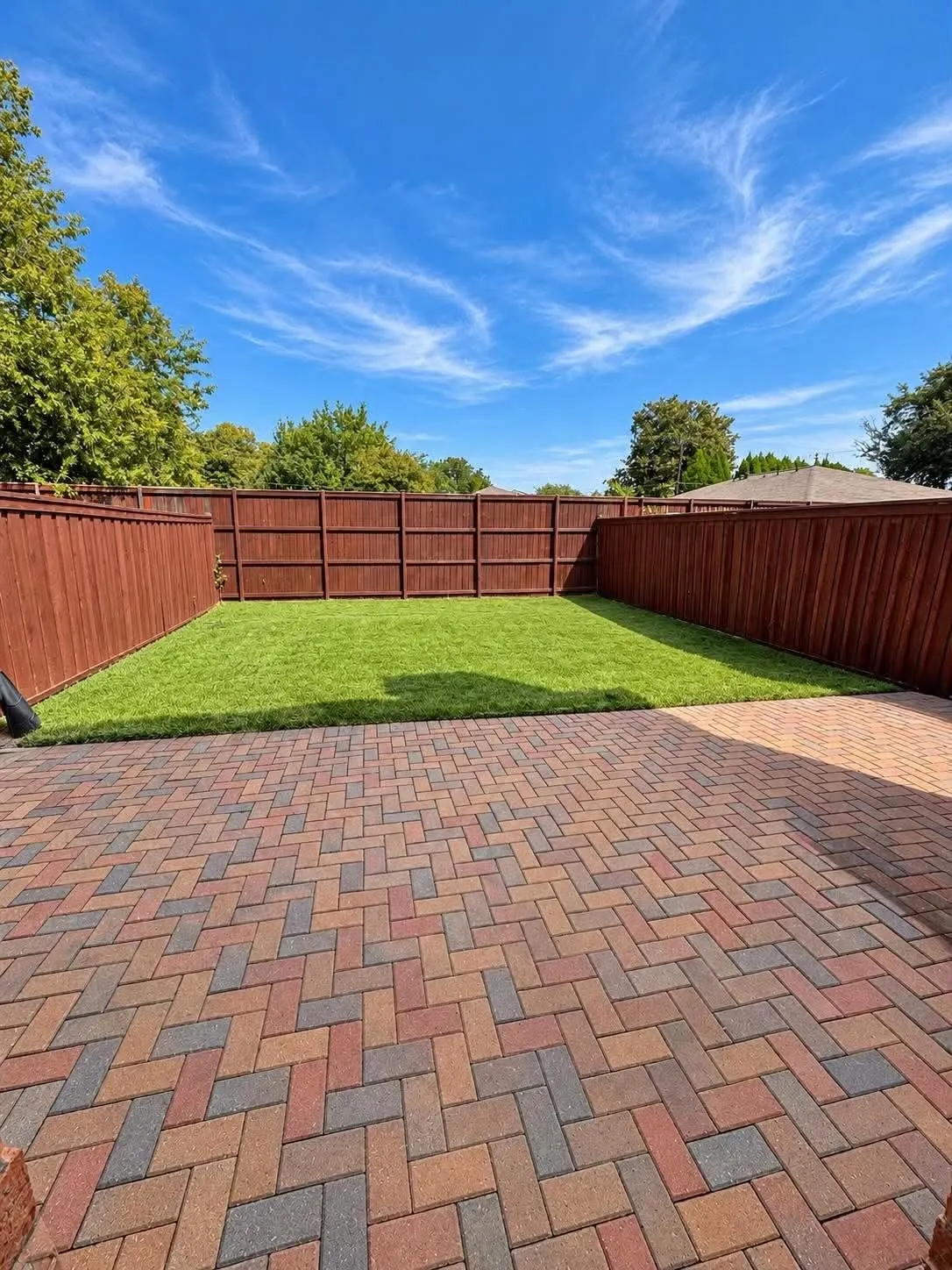 Paver patio with a herringbone pattern, manicured lawn, and privacy fencing