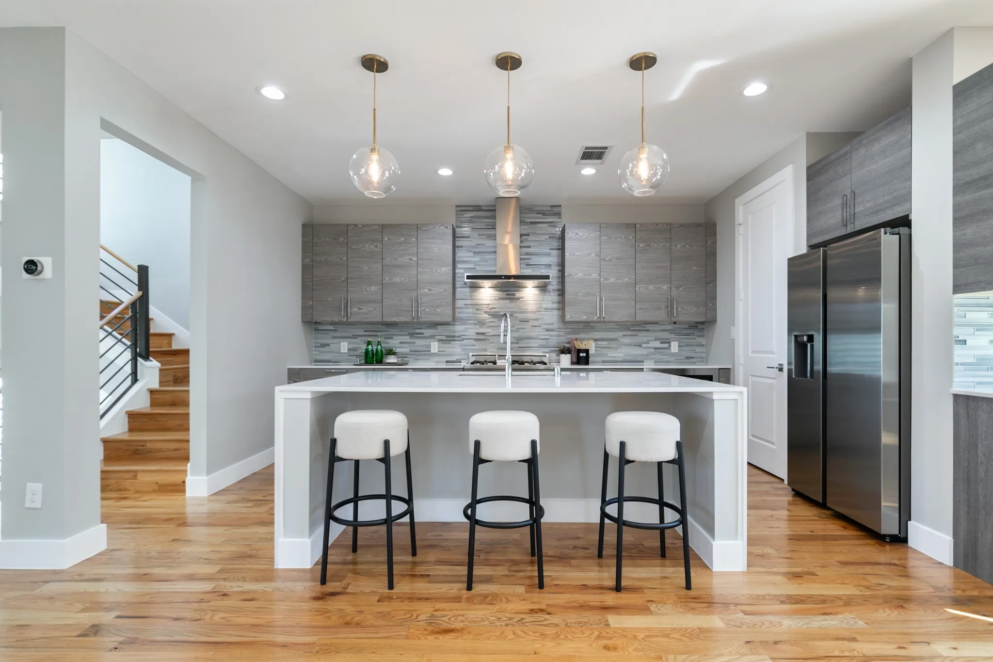 Hardwood flooring, stainless steel appliances, modern pendant lighting, gray cabinetry, and a spacious island