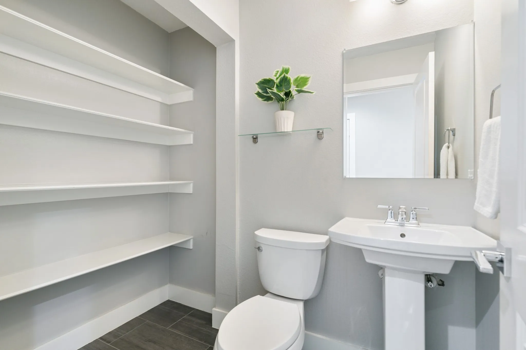 Pedestal sink with chrome fixtures, wall-mounted mirror, and dark tile flooring