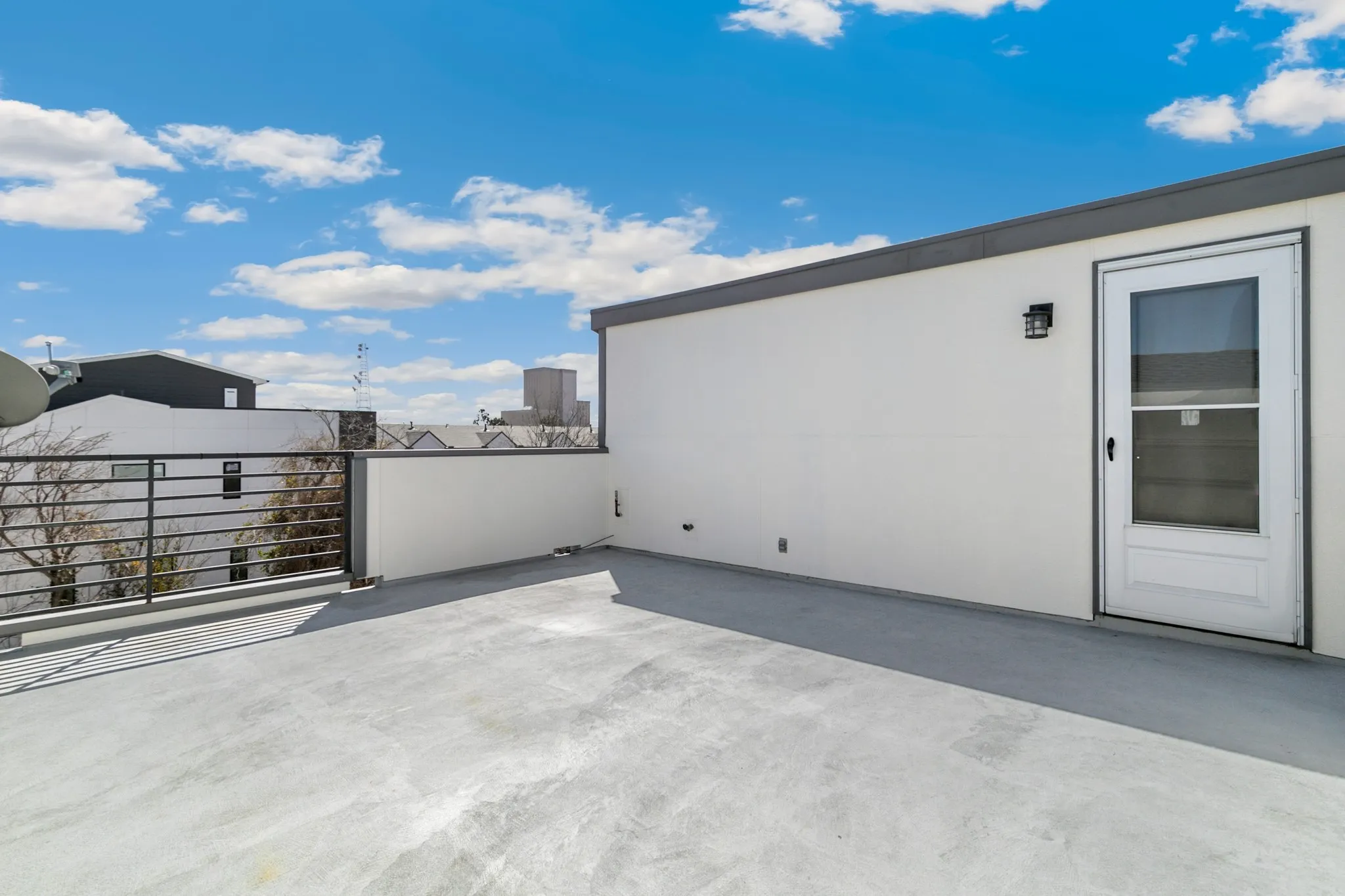 Expansive rooftop patio featuring a durable concrete surface, a black metal railing, and a white entry door with a screen