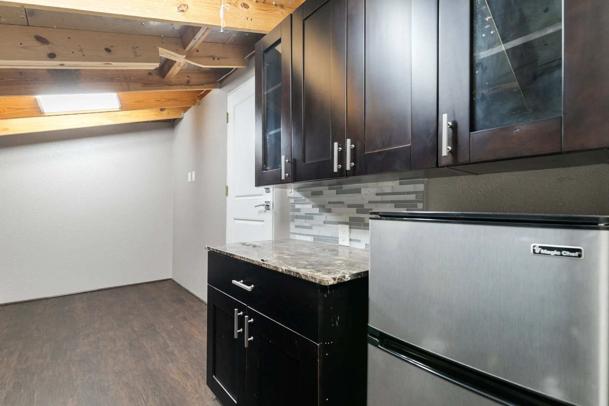 Wood-finish flooring, dark wood cabinetry with silver-tone hardware, and a mosaic tile backsplash