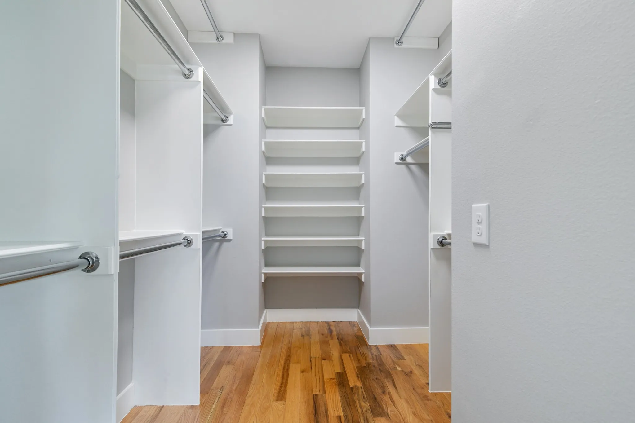 Walk-in closet with multiple hanging rods, extensive shelving, and wood-finish flooring