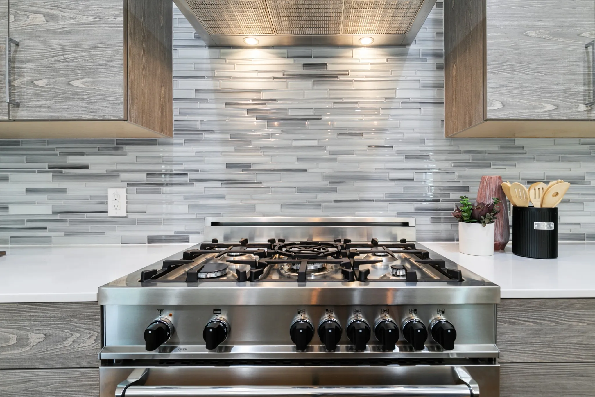 Stainless steel range and hood with integrated lighting, wood-finish cabinetry, white countertops, and glass tile backsplash