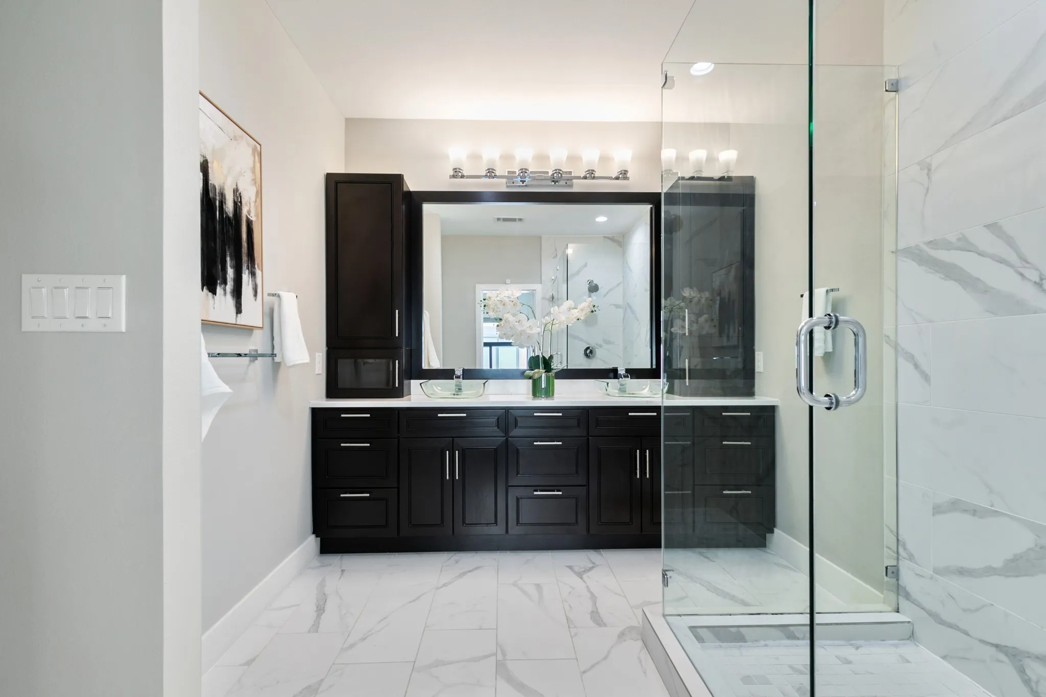Dual dark wood-finish vanities with vessel sinks, a spacious glass-enclosed shower, and large format white tile flooring