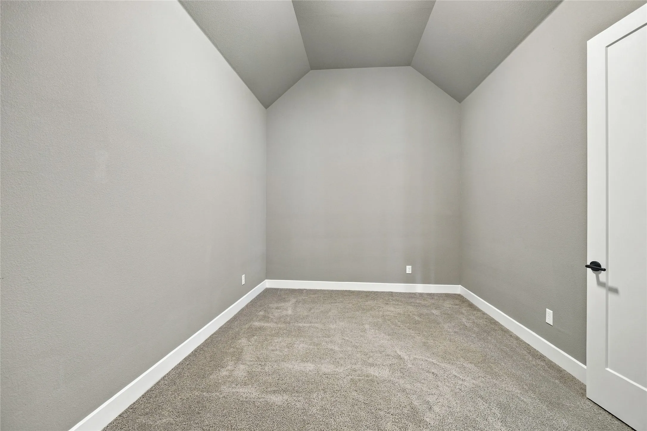 Vaulted ceiling, neutral wall paint, carpet flooring, white trim, and a contemporary door with matte black hardware