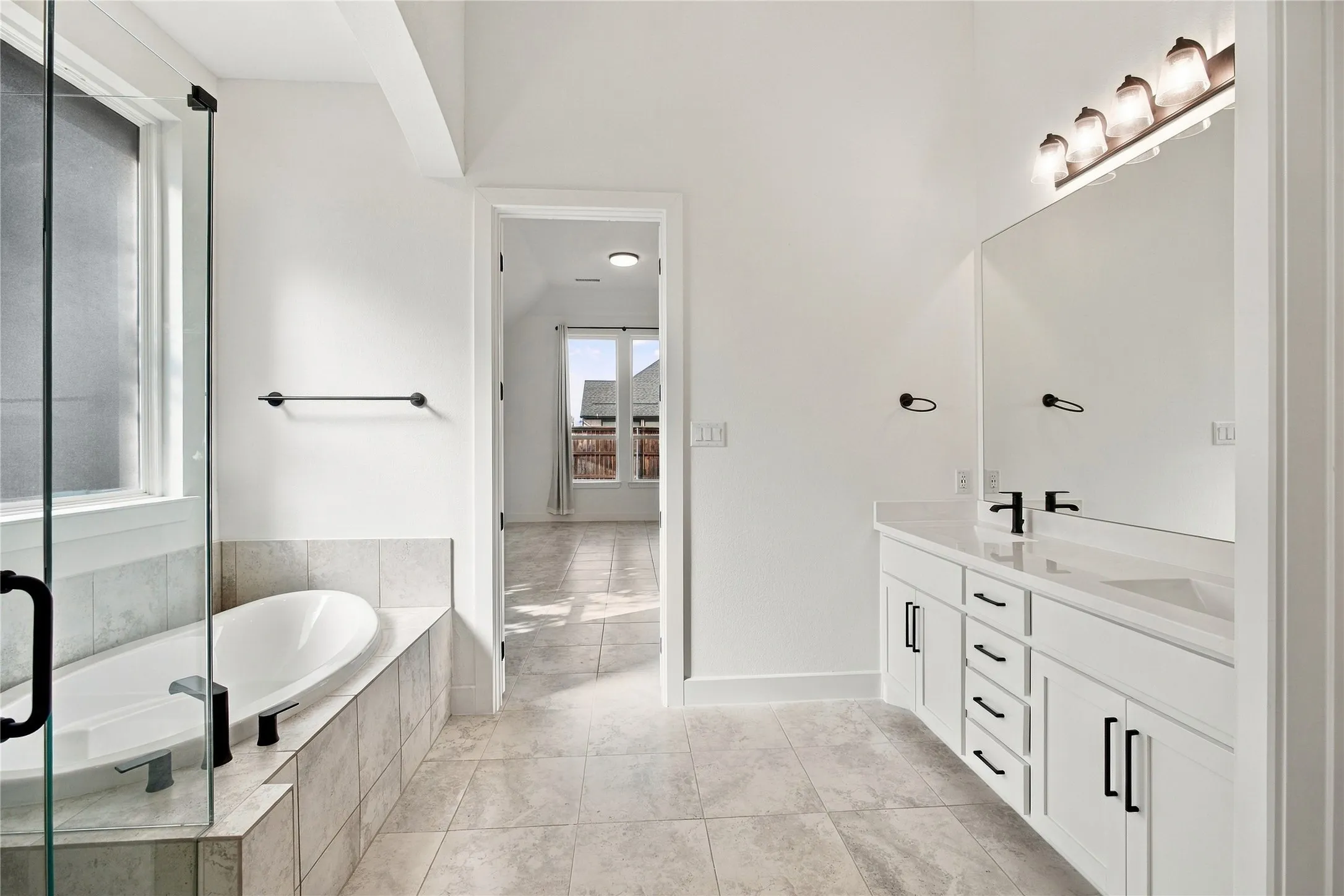White tile flooring, double vanity with white cabinetry, freestanding bathtub, glass-enclosed shower, and vaulted ceiling