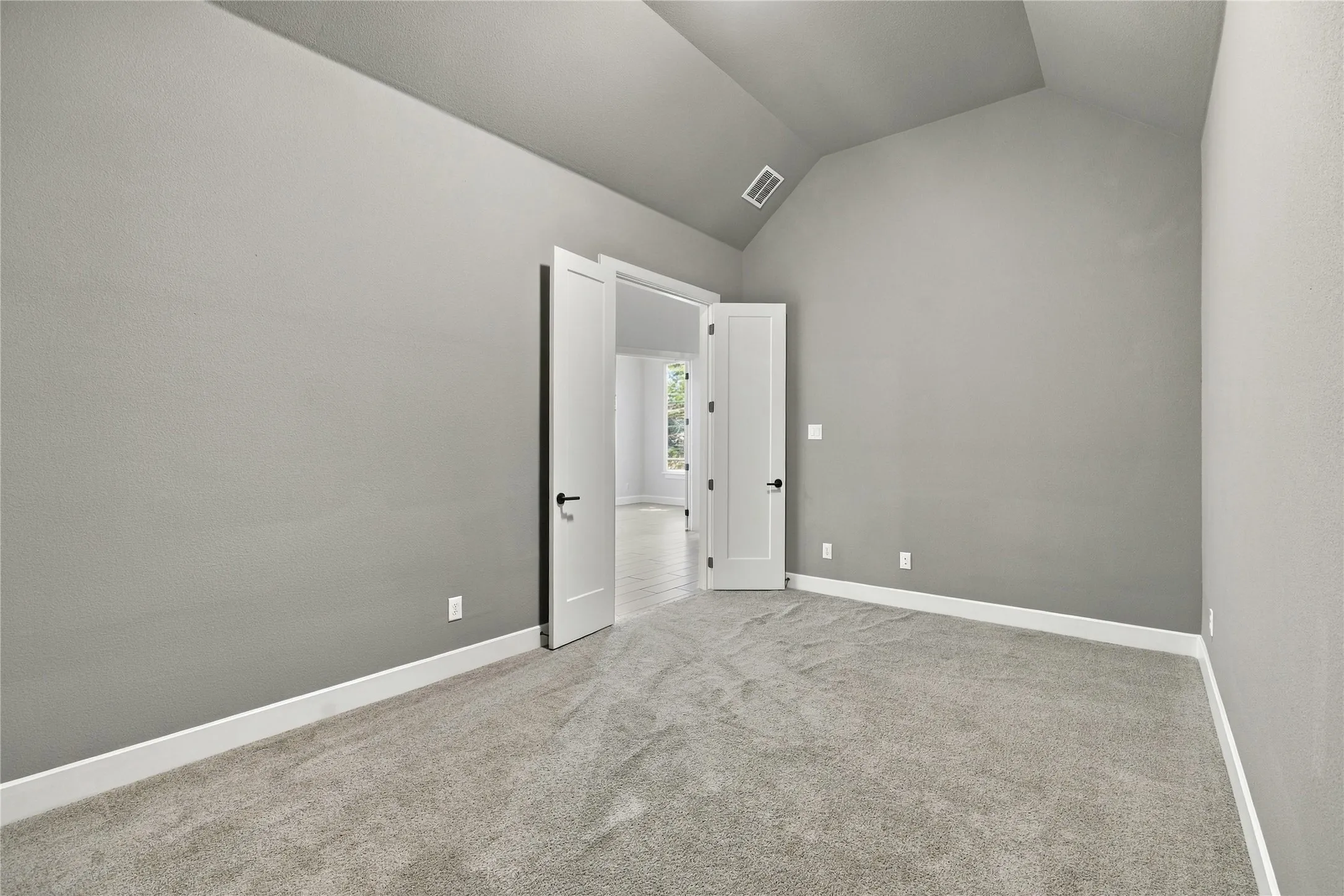 Vaulted ceiling, gray carpeting, neutral wall finishes, and white interior doors with dark hardware