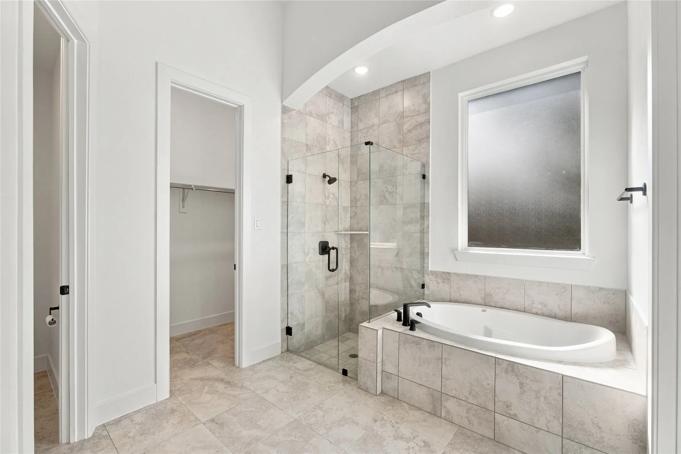 Spacious bathroom featuring a soaking tub, glass-enclosed shower, large privacy window, and tile flooring