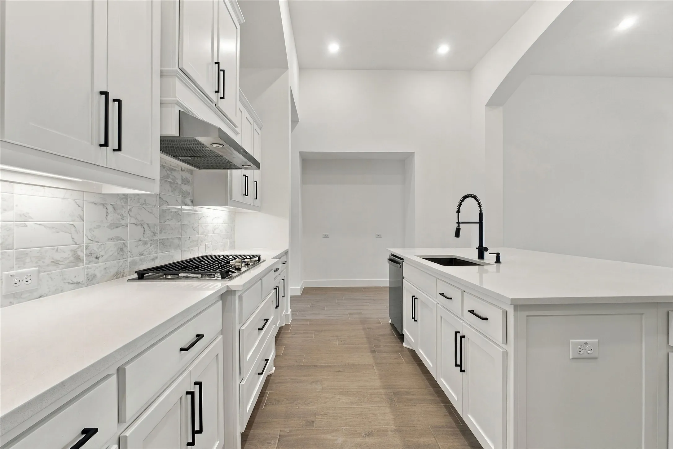 White shaker cabinetry, light-toned wood-finish flooring, white countertops, built-in gas range, and a black gooseneck faucet