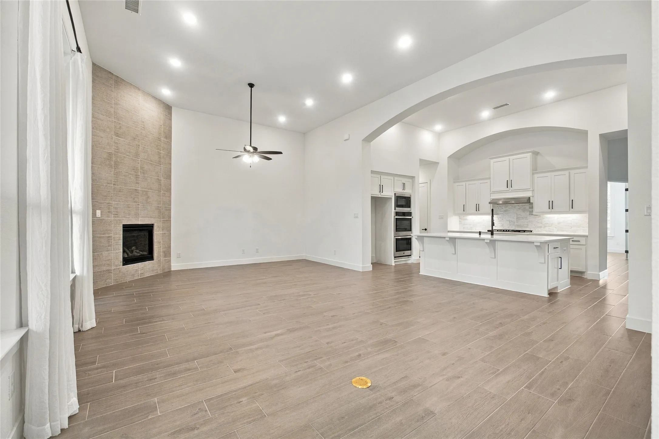 Vaulted ceilings with recessed lighting, floor-to-ceiling tile fireplace, wood-finish flooring, white kitchen cabinetry, and a central kitchen island