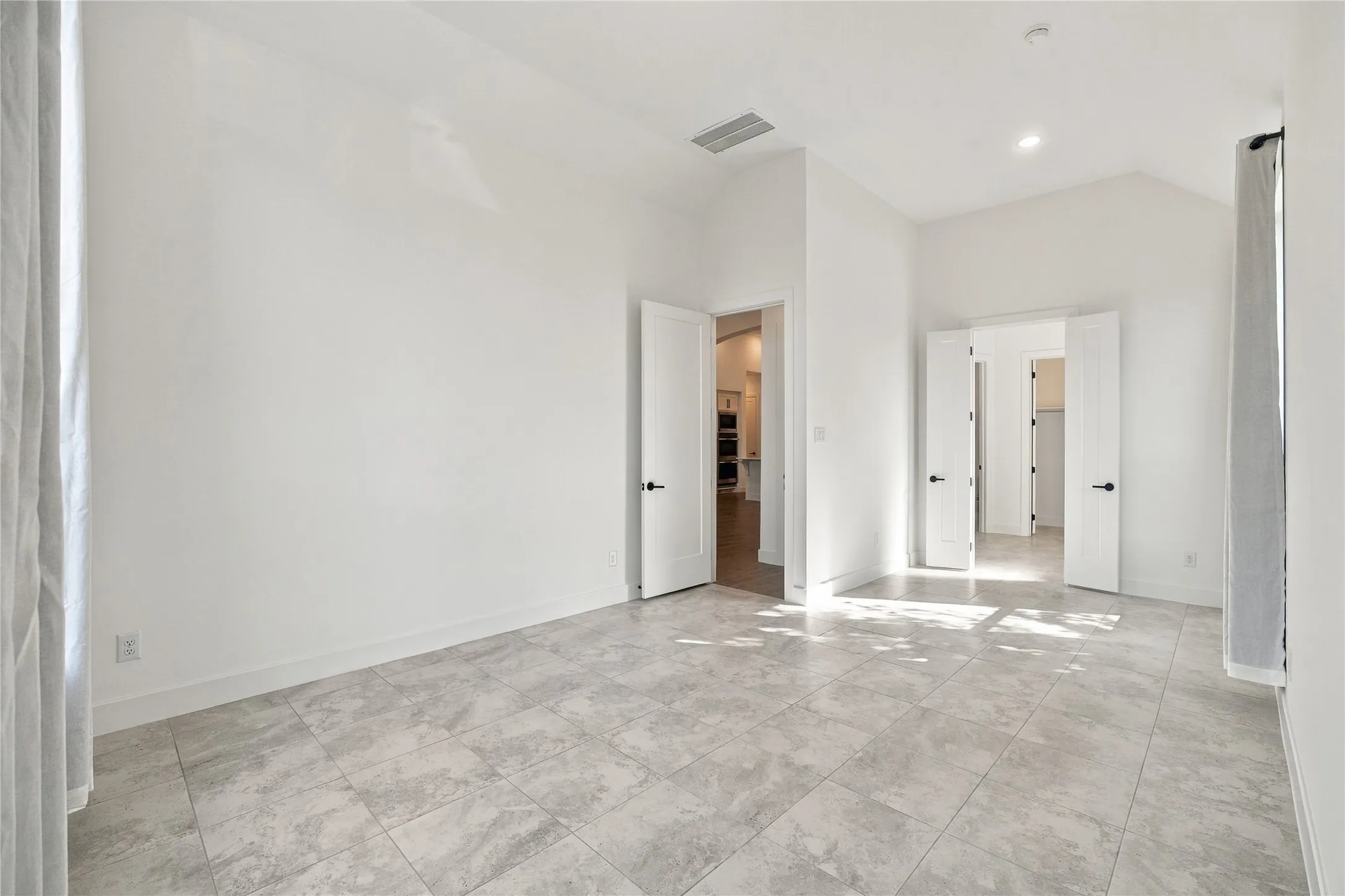 Spacious room featuring vaulted ceilings, recessed lighting, tile flooring, and multiple doorways with modern hardware