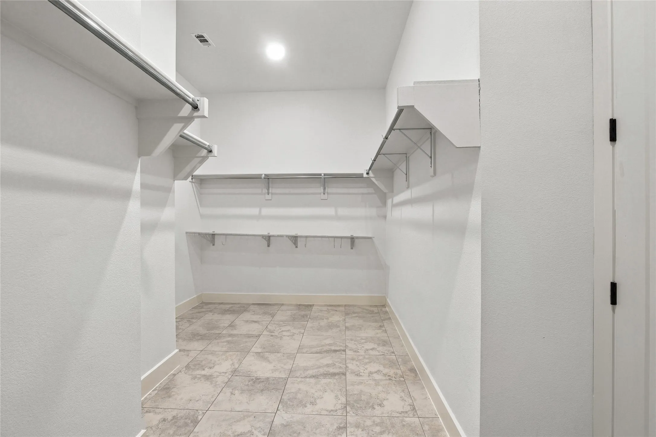 Walk-in closet featuring built-in shelving, hanging rods, recessed lighting, and tile flooring