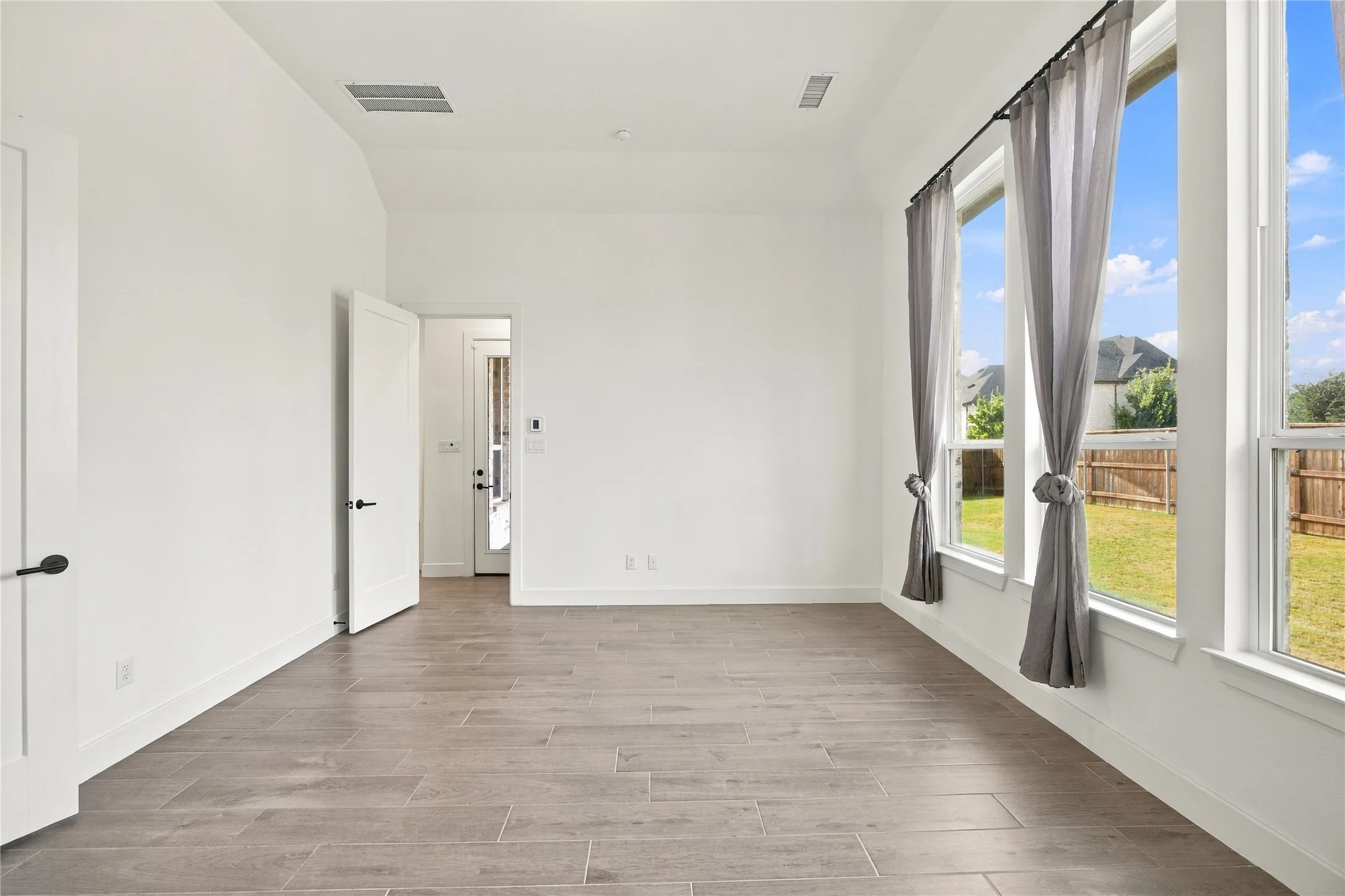 Vaulted ceiling, wood-finish flooring and multiple windows with backyard views