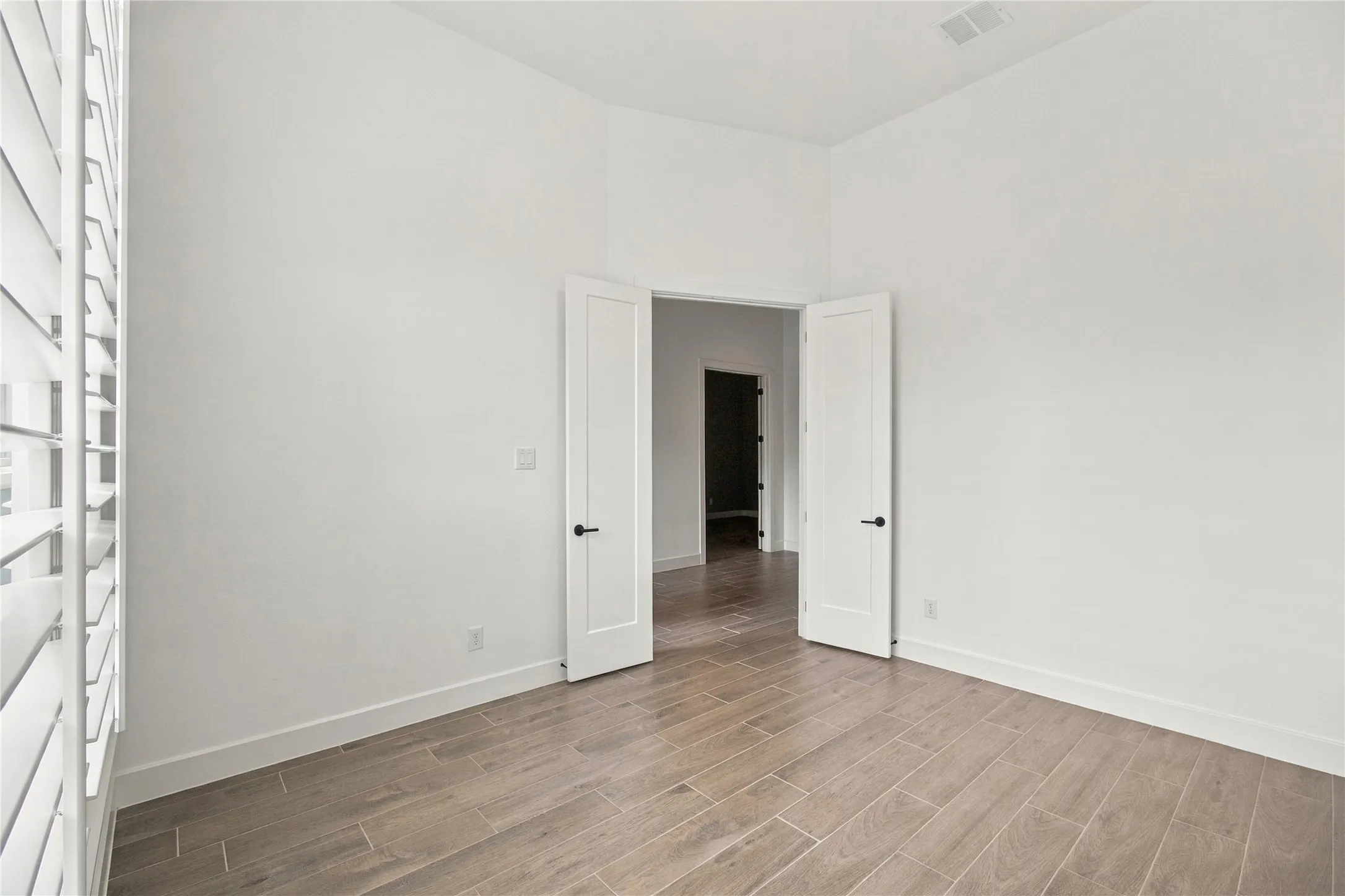 Wood-finish tile flooring, white interior walls, white plantation shutters, and a white interior door with black hardware
