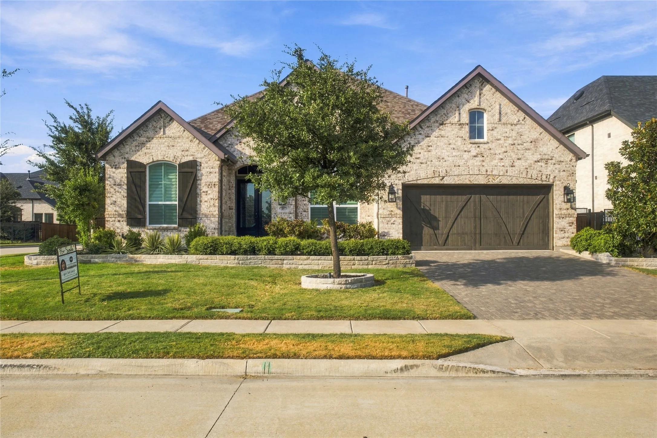 Full bricks residence featuring stone landscape borders front lawn with mature landscaping, a paved driveway, and a two-car garage with a wood-finish door