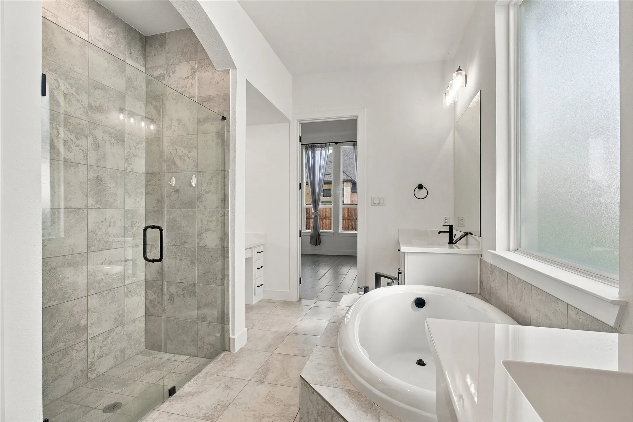 Spacious bathroom featuring a glass-enclosed shower, built-in soaking tub, single vanity with a solid surface countertop, and large frosted window