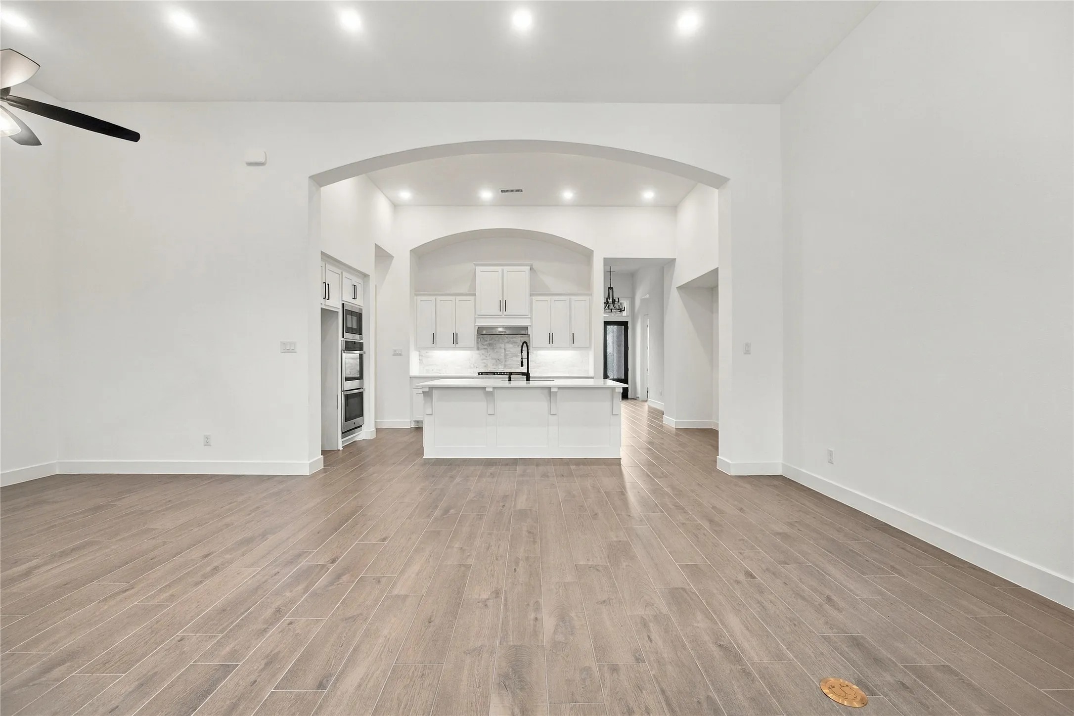 Spacious open-concept interior featuring wood-finish flooring, recessed lighting, and an arched entry to the kitchen