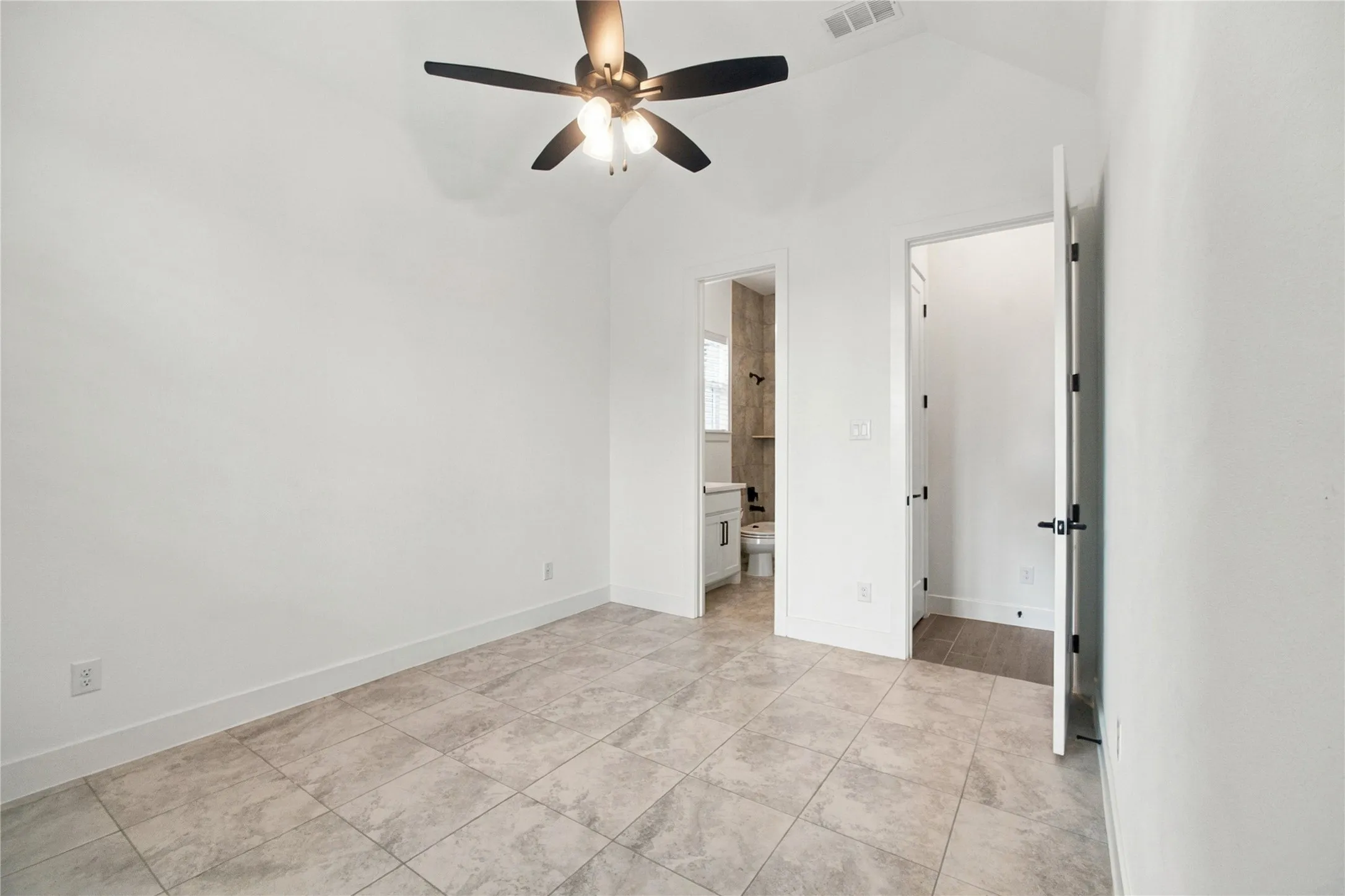 Vaulted ceiling, ceiling fan with integrated lighting, tiled flooring, white walls, and a white door with black hardware