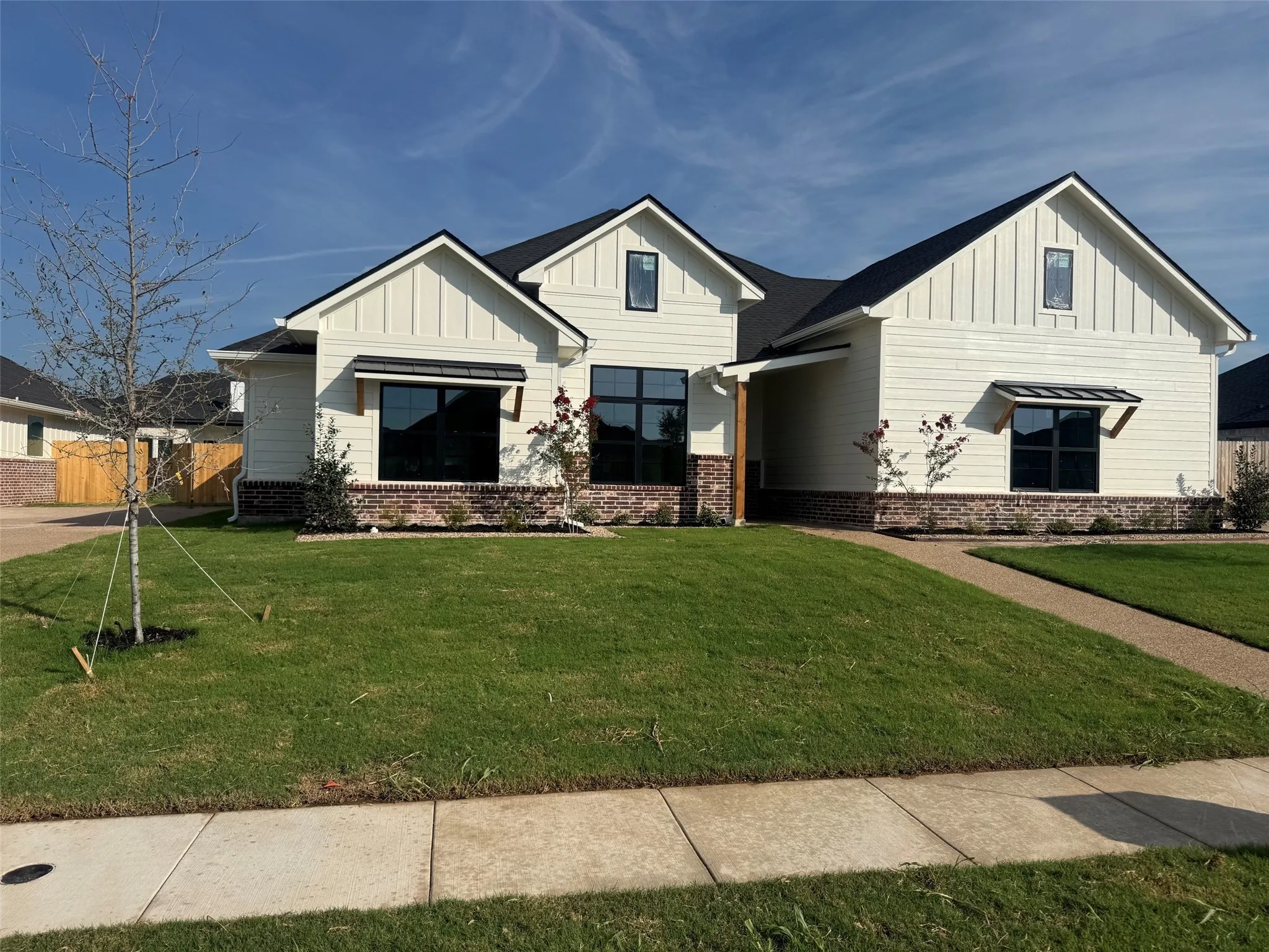 Modern farmhouse exterior featuring board and batten siding, dark framed windows, brick wainscoting, and a covered entry