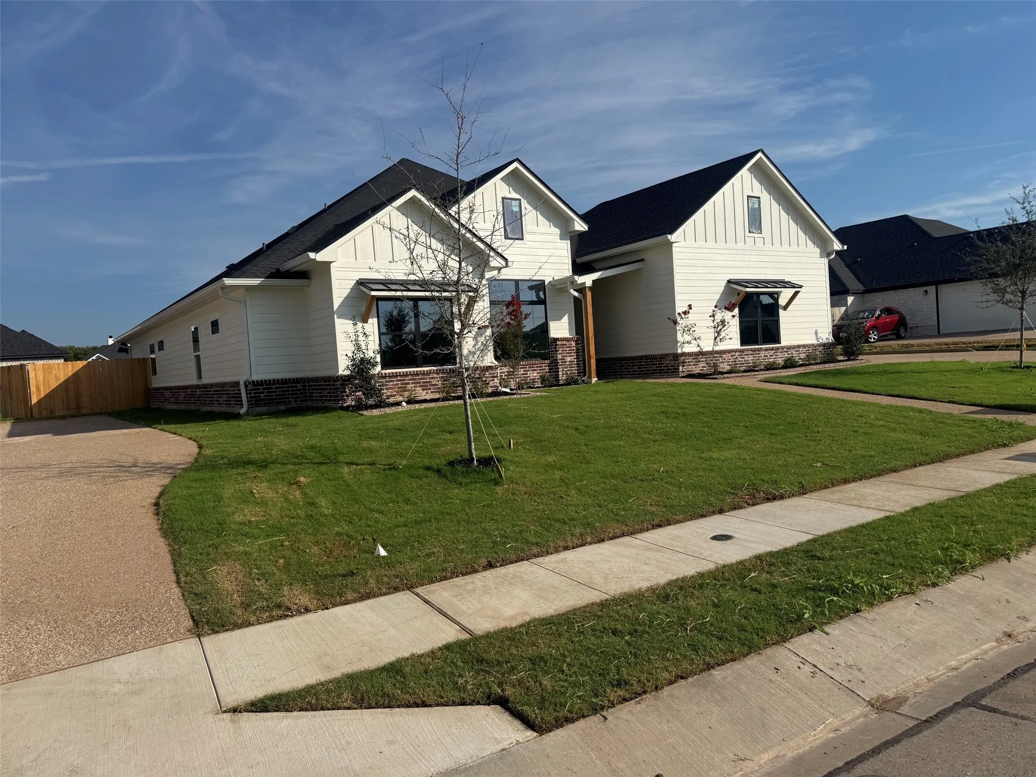 Contemporary exterior featuring board and batten siding, brick detailing, dark roof, expansive lawn, and an exposed aggregate driveway