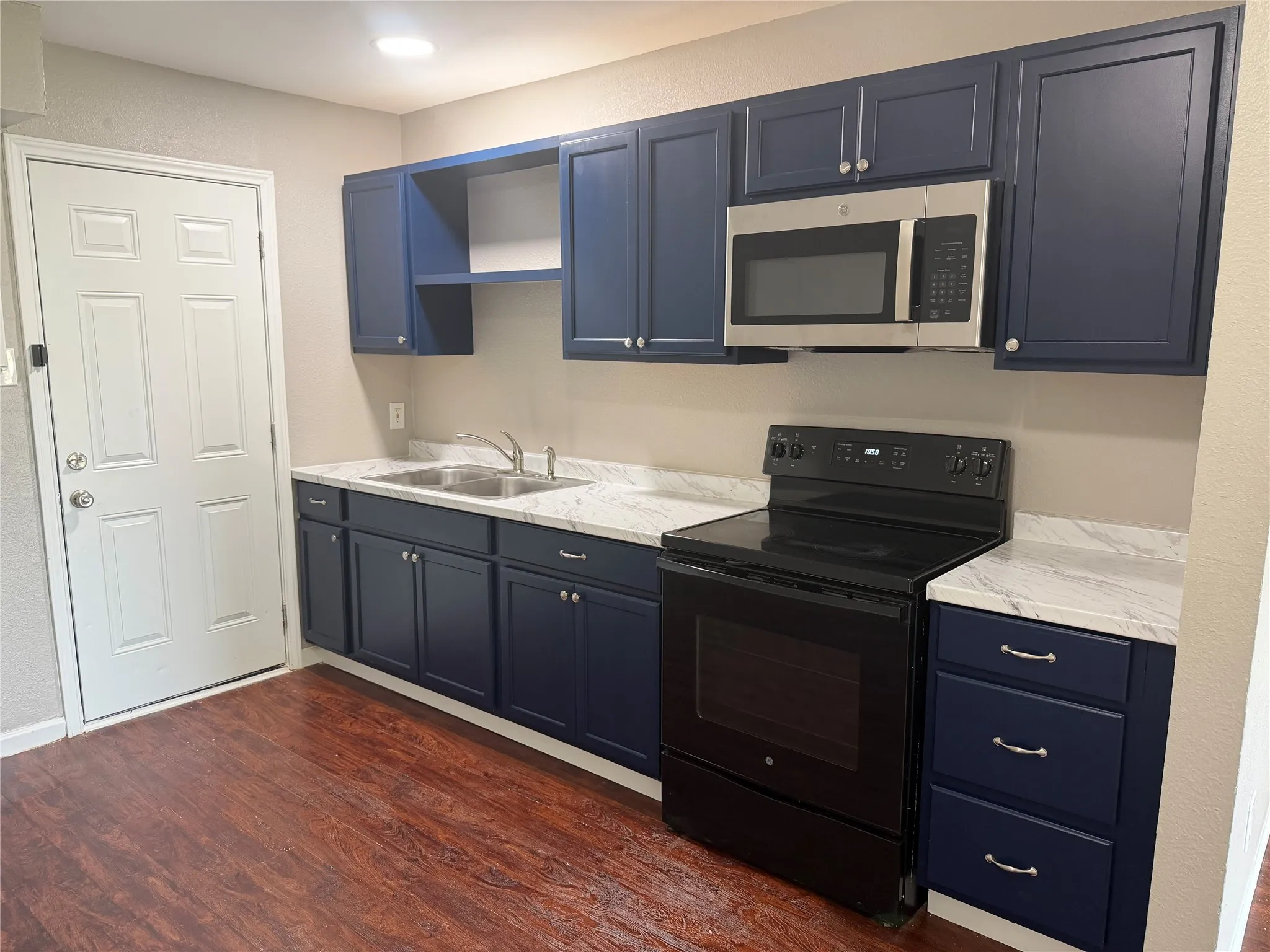 Navy blue cabinetry, dual basin stainless steel sink, wood-finish flooring, electric range, stainless steel microwave