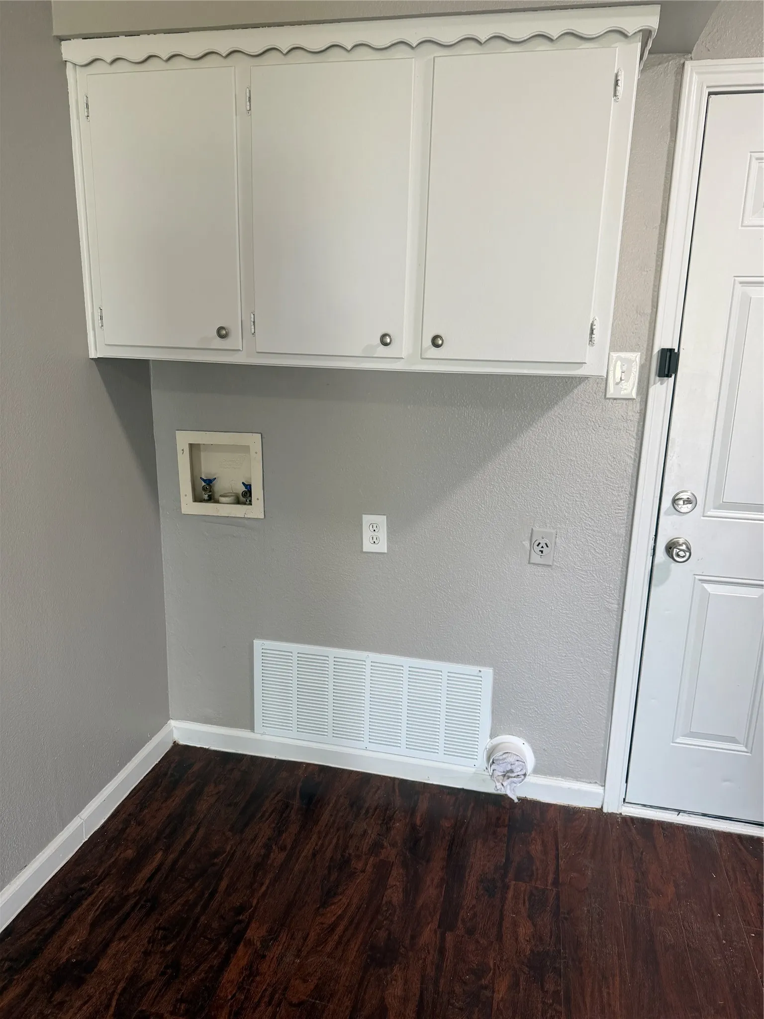 Wood-finish flooring with white baseboards, white upper cabinetry, and a white paneled door