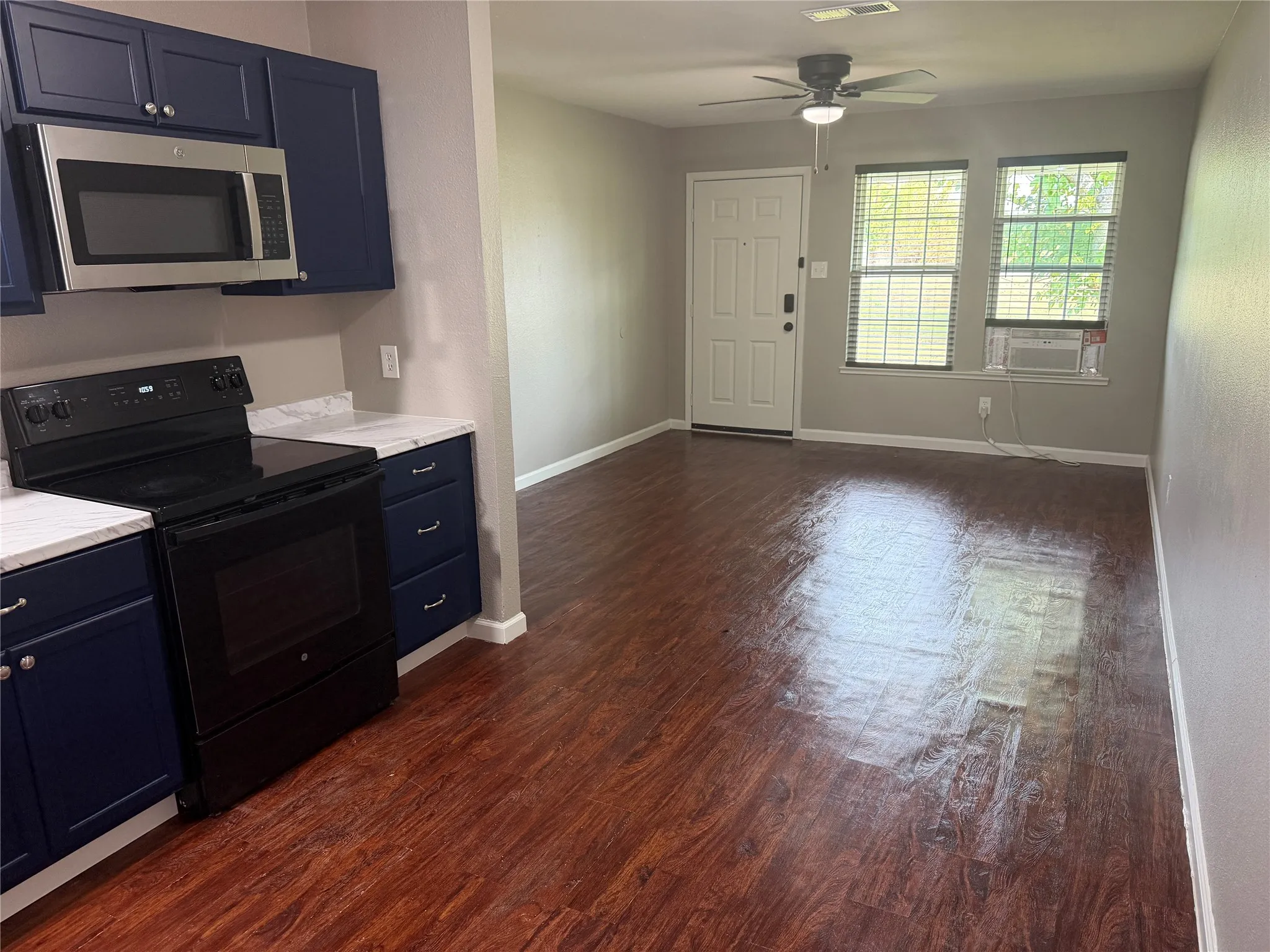 Kitchen with dark wood-finish flooring, dark blue cabinetry, white countertops, and stainless steel microwave
