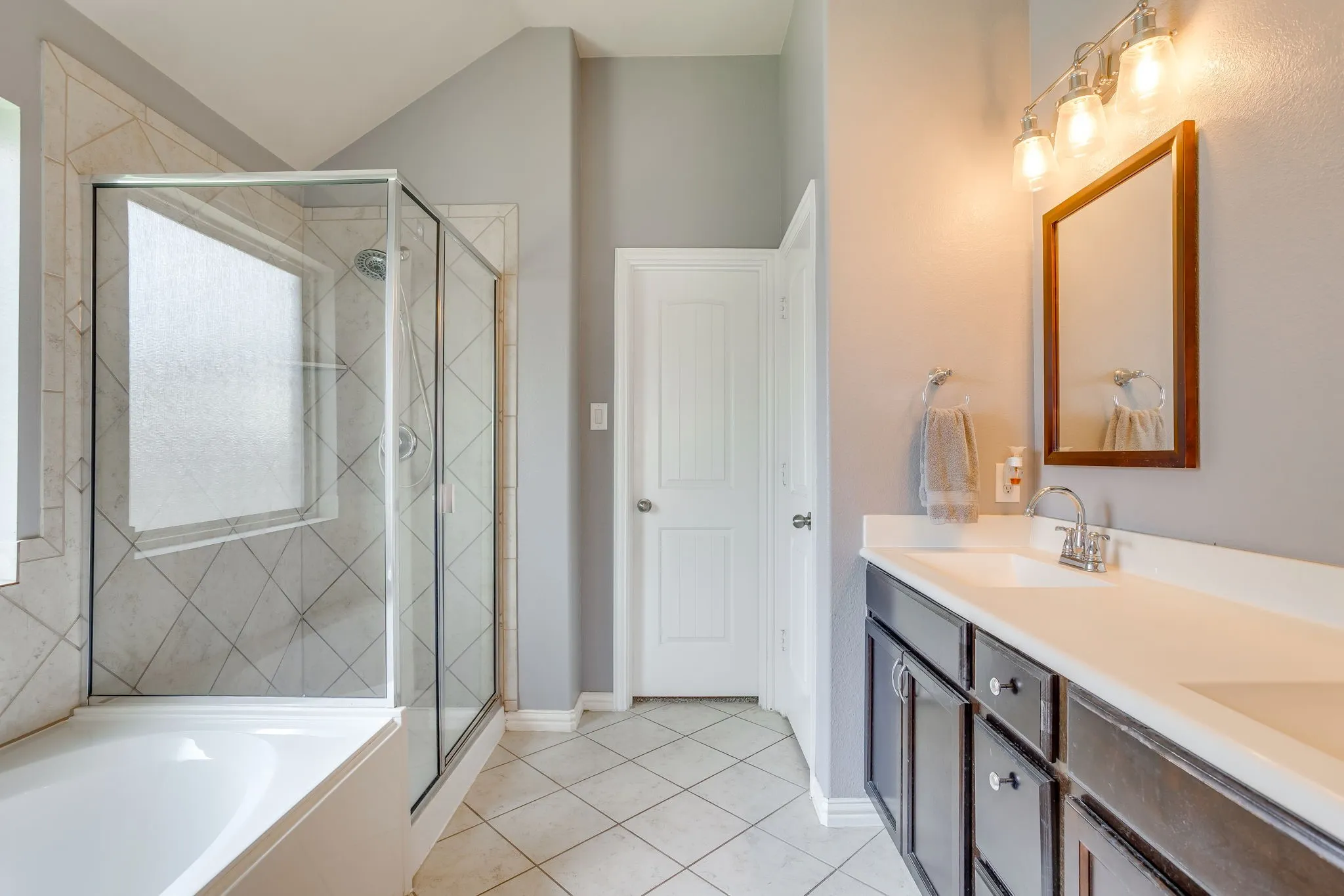 Built-in bathtub with glass enclosure, tiled shower surround, dual sink vanity with white countertop, and tiled flooring