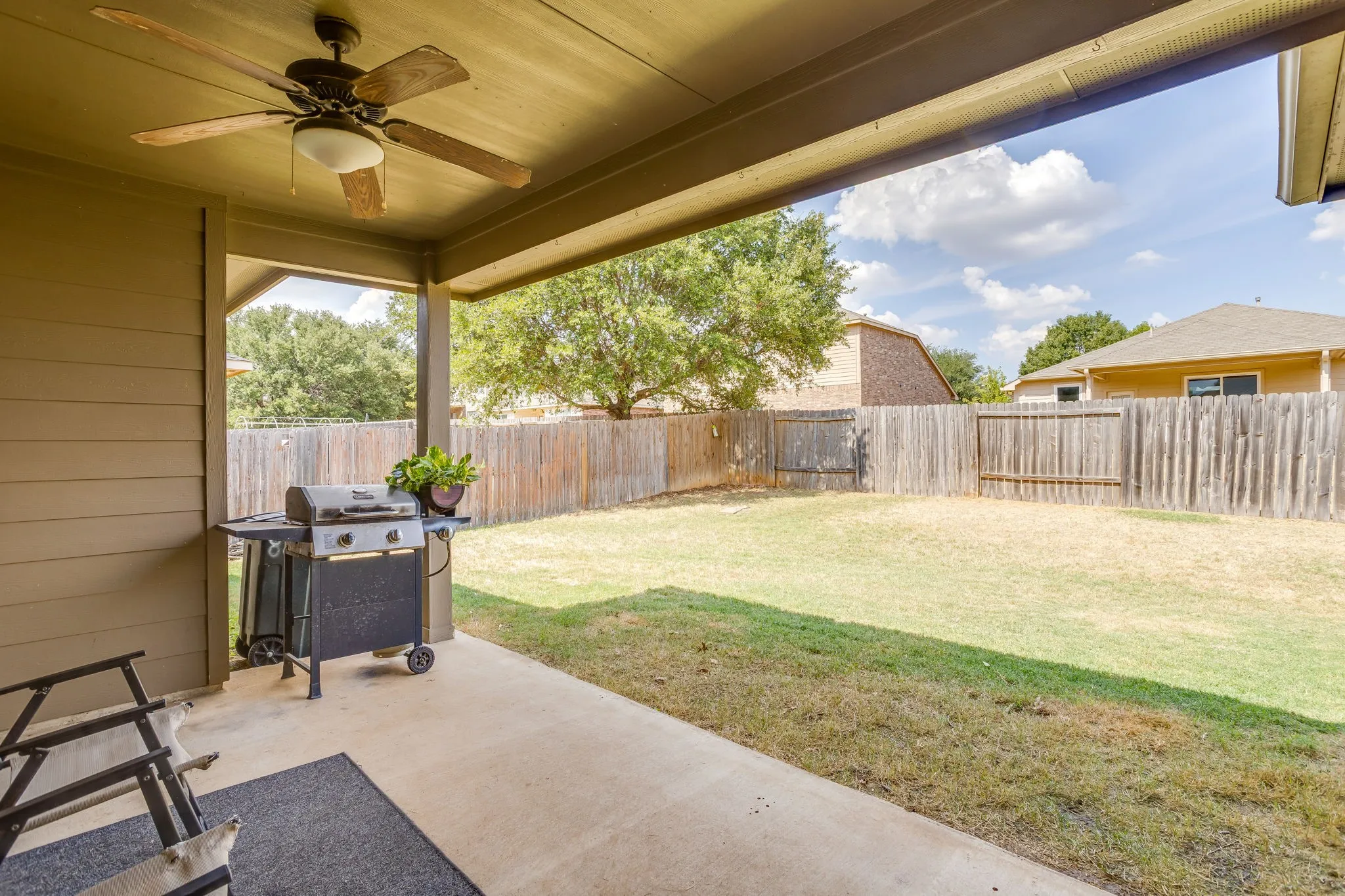 Covered outdoor patio with a ceiling fan, concrete flooring, and fenced backyard with mature trees