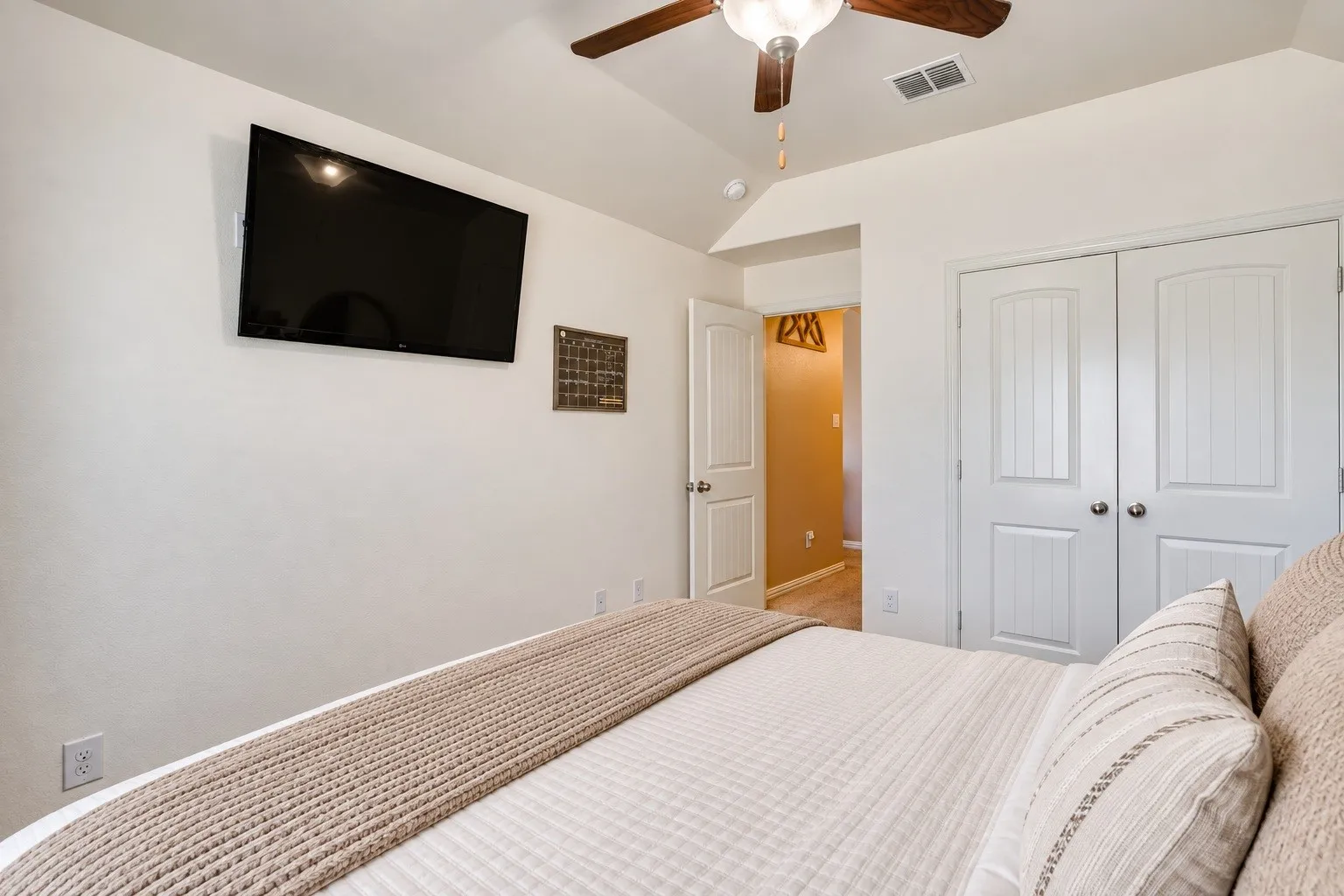 Vaulted ceiling featuring a ceiling fan, white paneled doors, and a wall-mounted television. Picture virtually edited