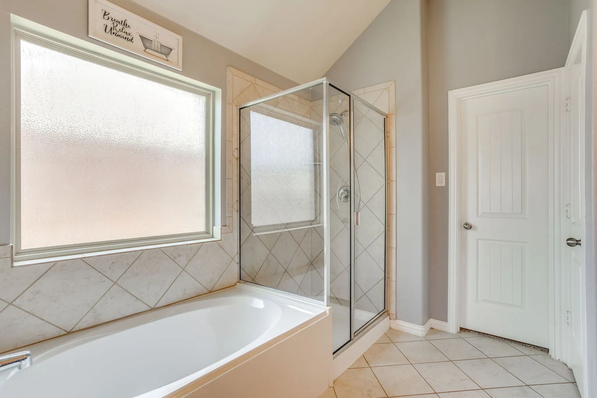 Soaking tub, glass-enclosed shower, tiled flooring, tiled surround, and a frosted window