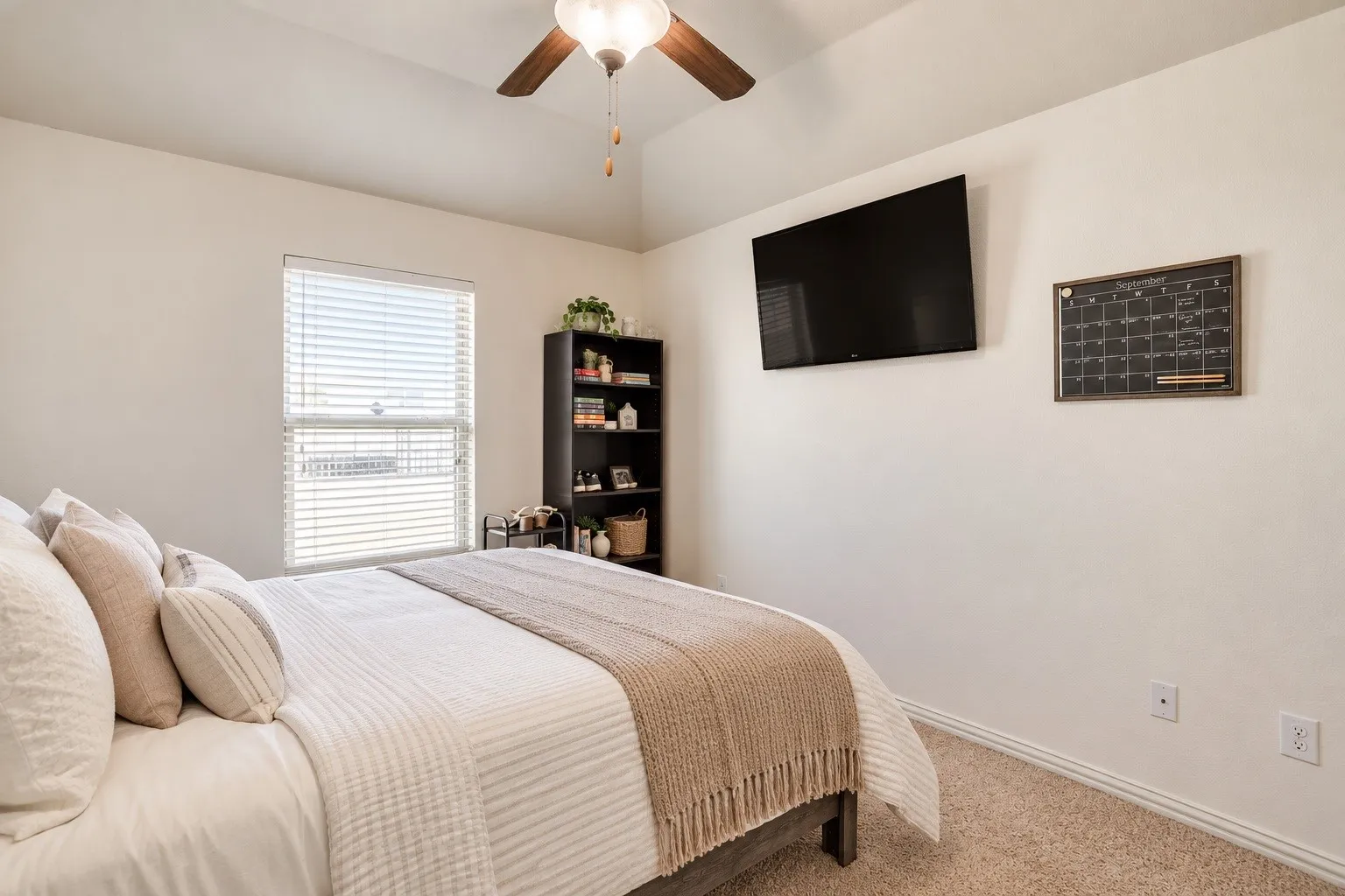 Carpeted flooring, vaulted ceiling, ceiling fan with integrated lighting, built-in shelving, and window with blinds. Picture virtually edited