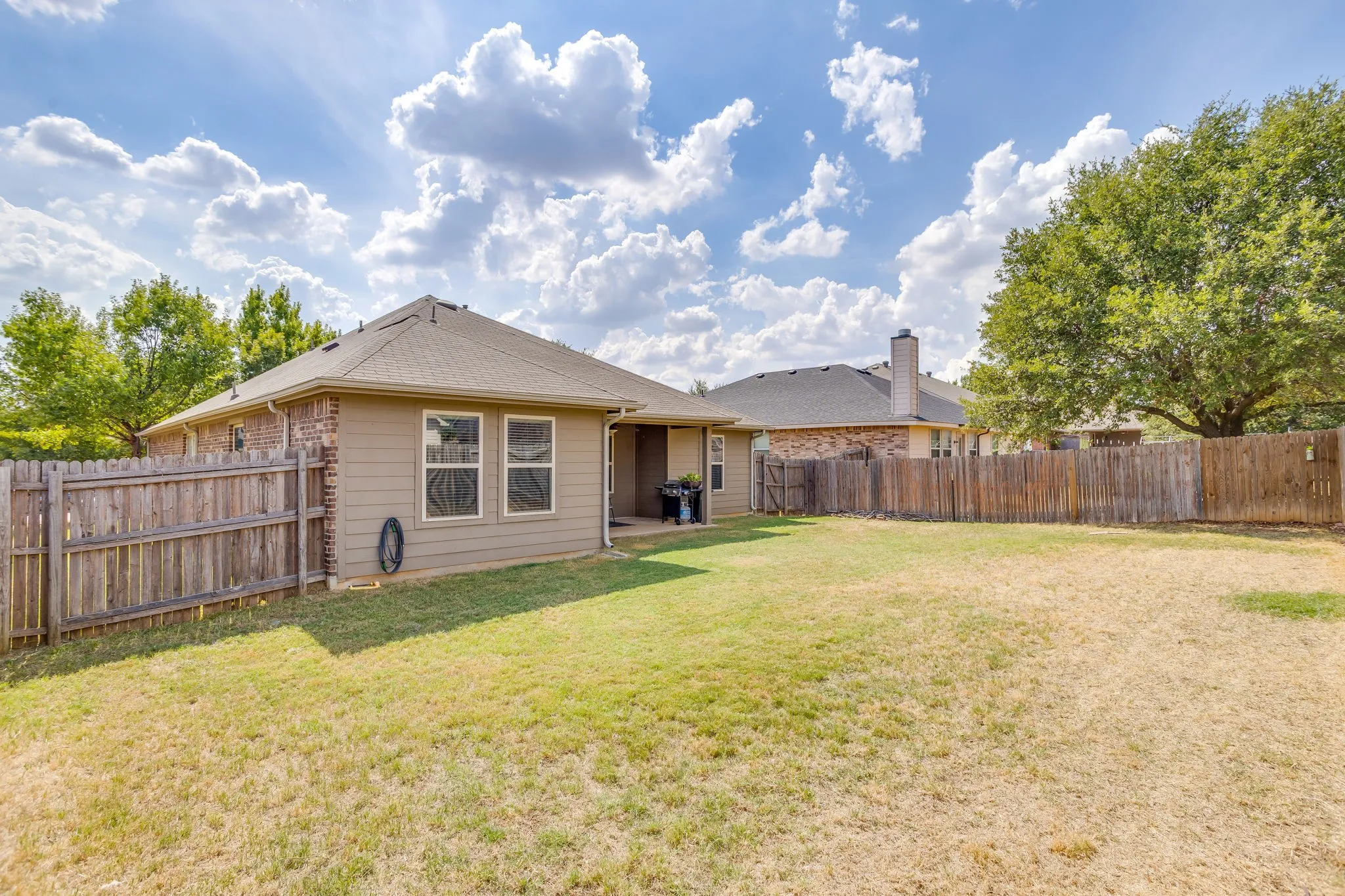 Expansive backyard featuring a wood privacy fence, a covered patio, and mature trees