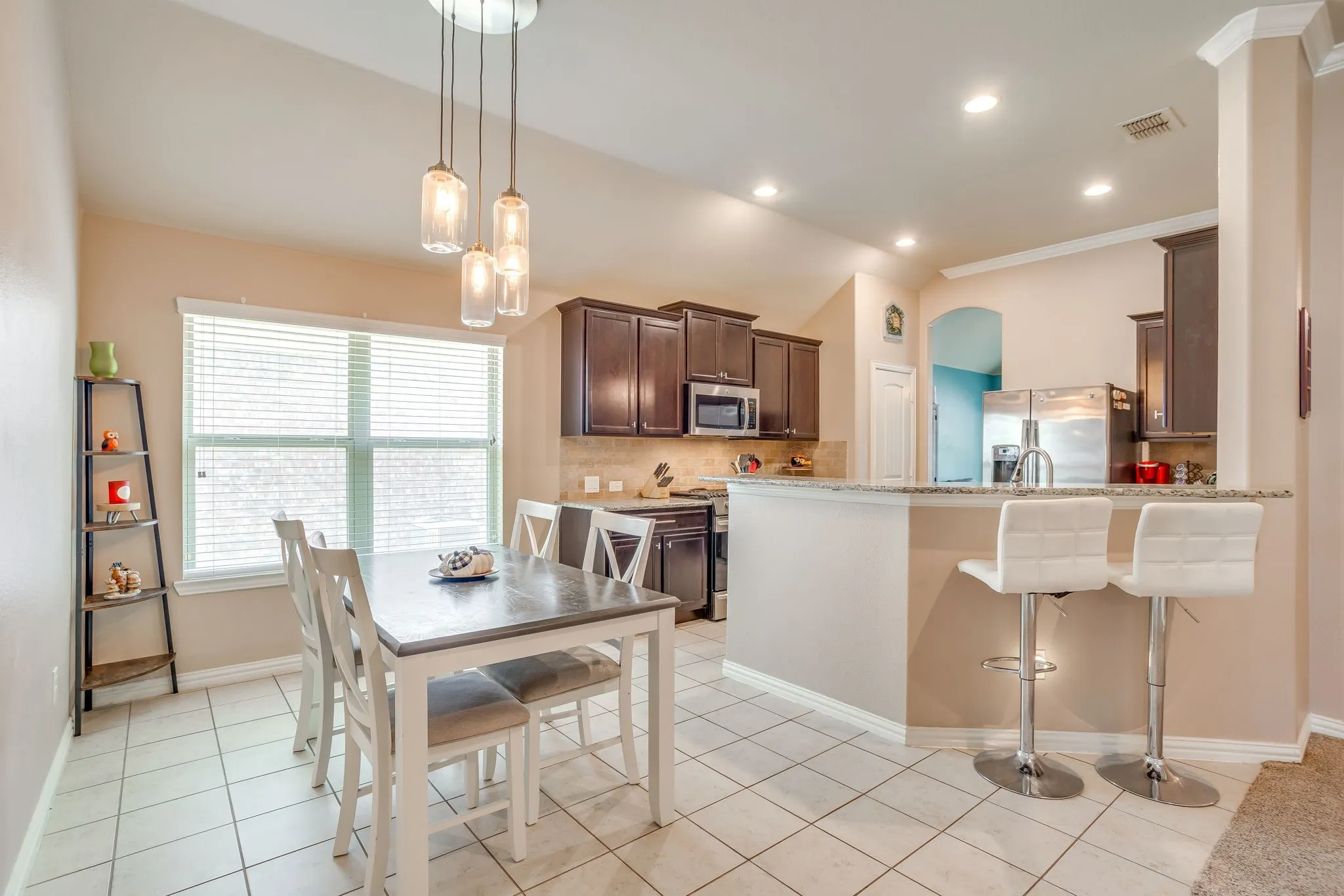 Open-concept kitchen and dining area featuring tile flooring, dark wood cabinetry, a breakfast bar with a stone-finish countertop, and recessed lighting