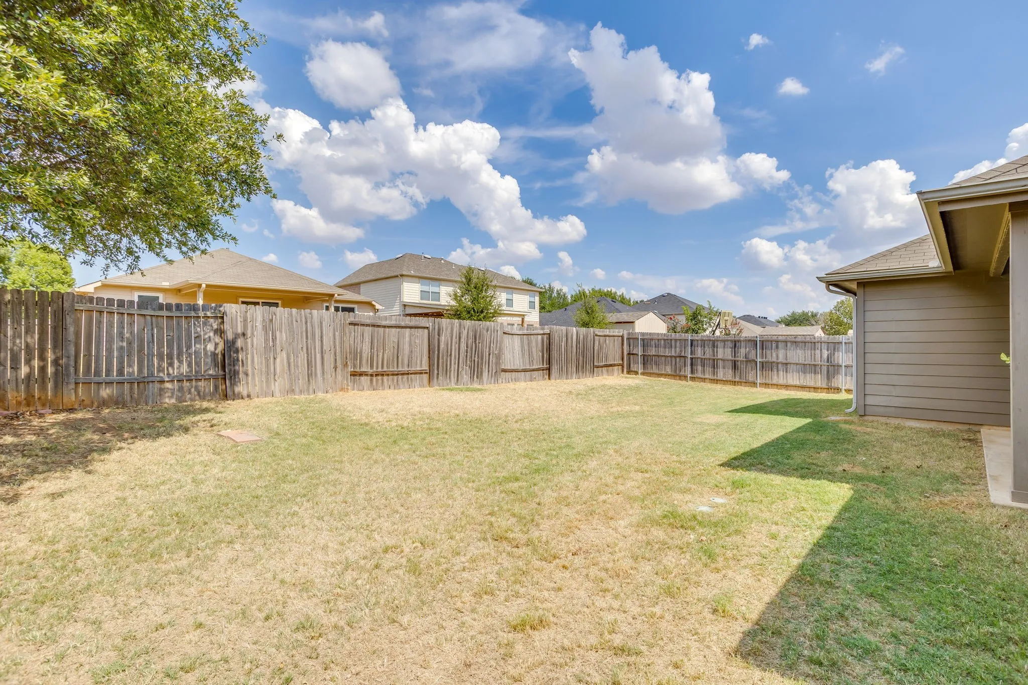 Expansive backyard featuring a wood privacy fence and a partial concrete patio