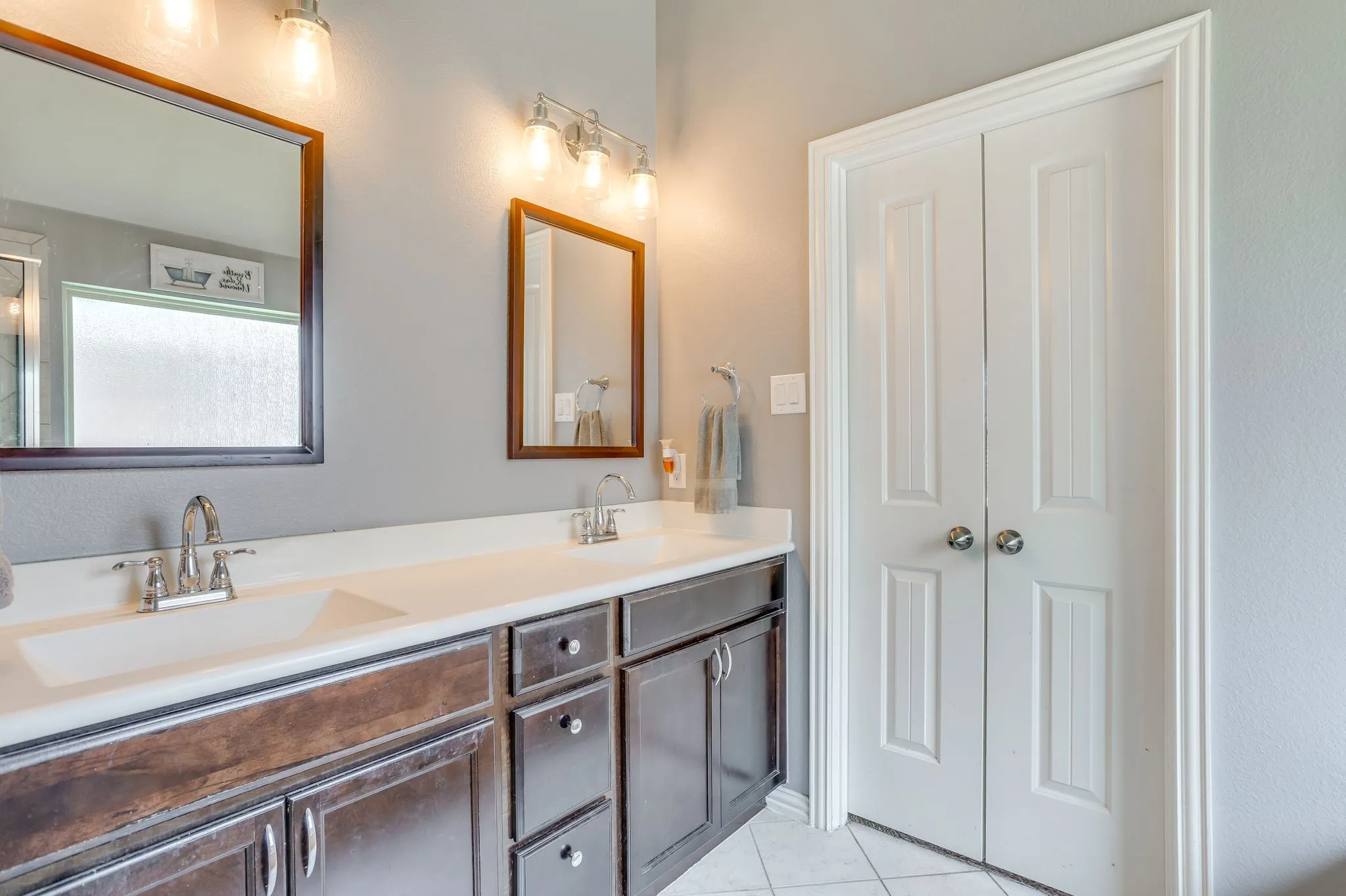 Double vanity with integrated sinks, dark wood-finish cabinetry, chrome fixtures, and dual framed mirrors