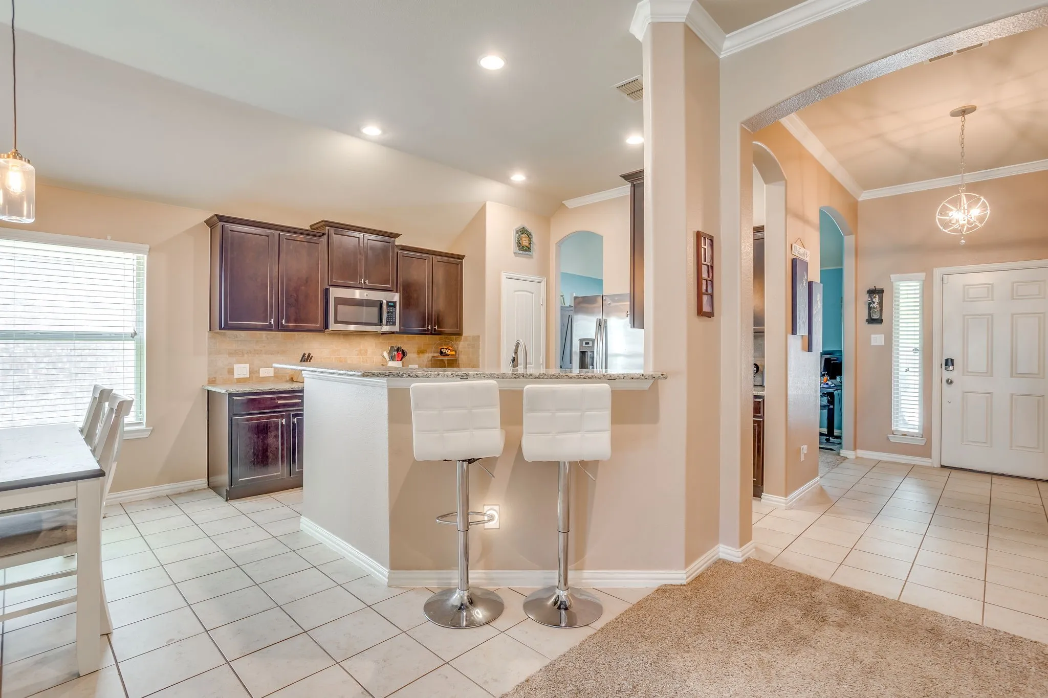 Kitchen featuring dark wood cabinetry, stainless steel microwave, stone backsplash, and a breakfast bar with a light-colored countertop
