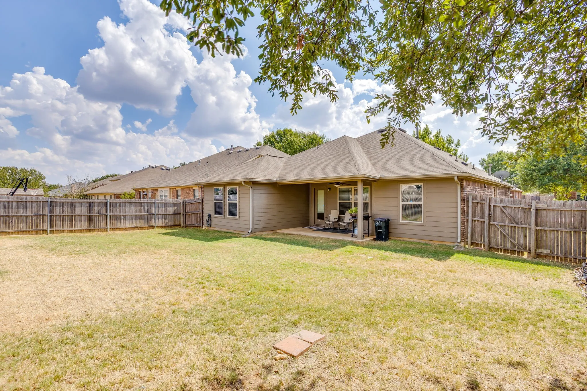 Expansive backyard featuring a wood fence, covered patio, and mature trees