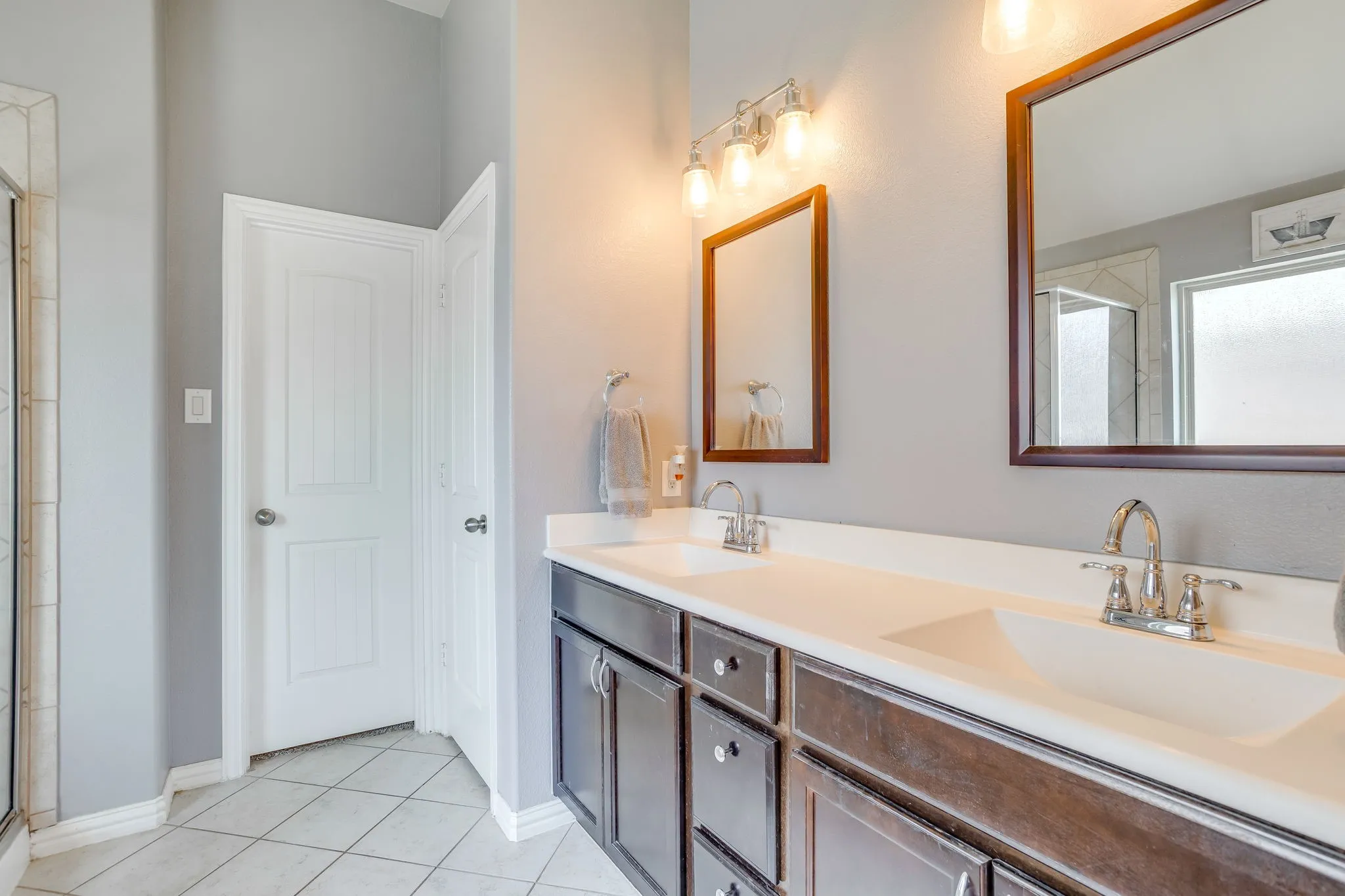 Double vanity with integrated sinks, dark wood-finish cabinetry, bright overhead lighting, and framed mirrors