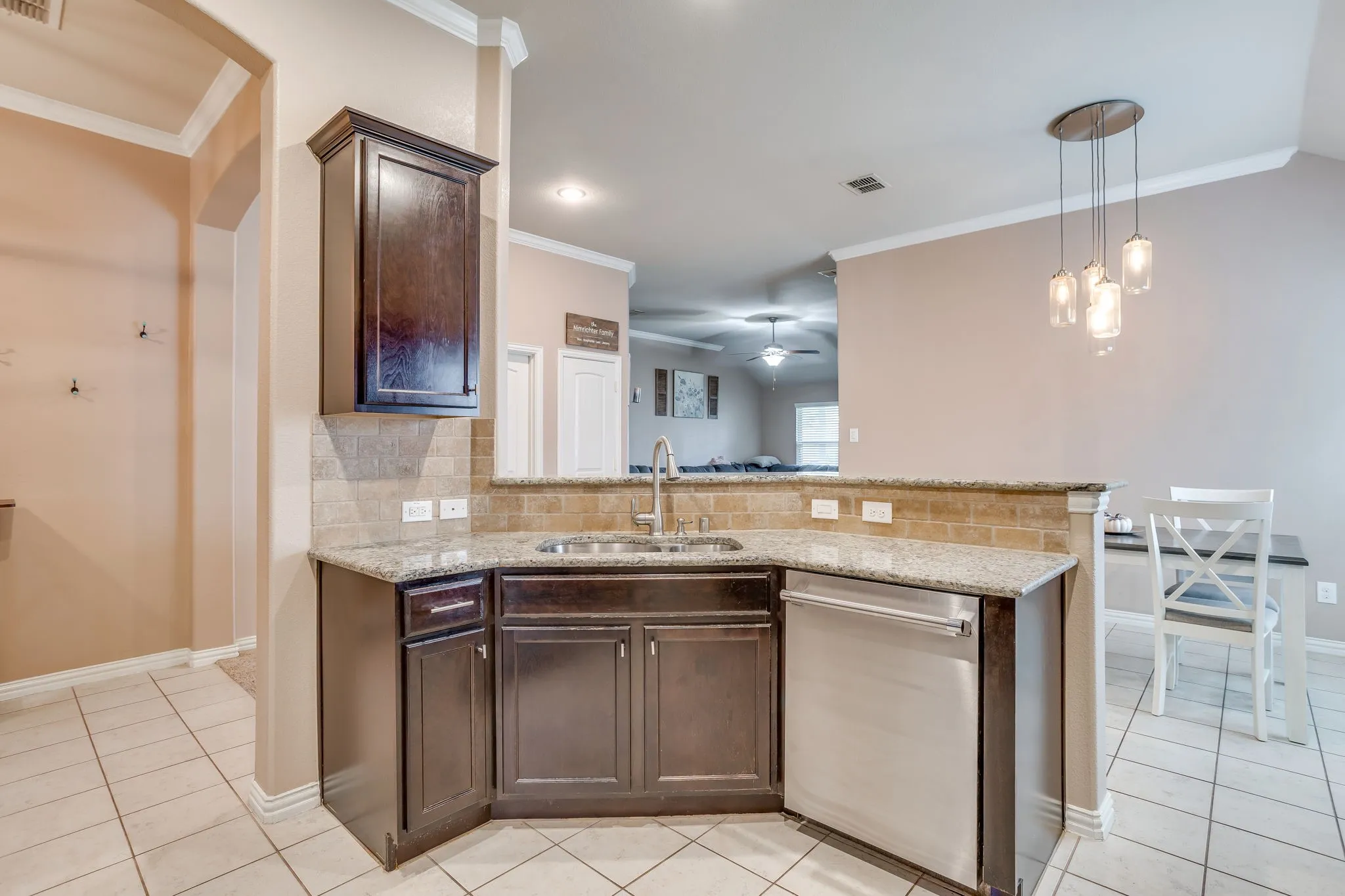 Kitchen featuring granite countertops, wood cabinetry, stainless steel dishwasher, tile backsplash, and a pendant light fixture